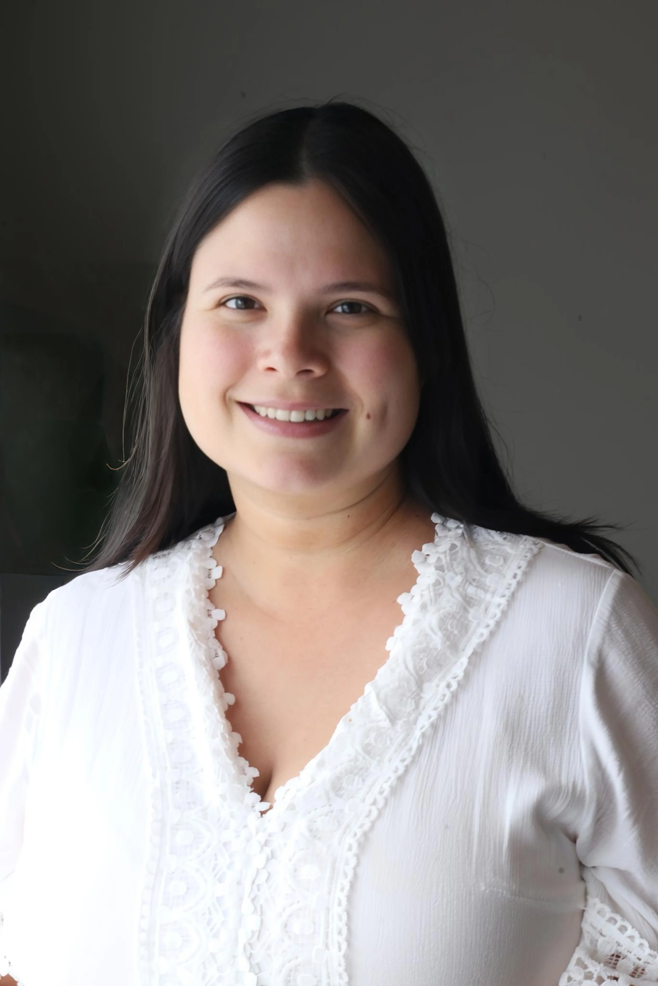 Retrato de una mujer con cabello negro y sonrisa, vestida con blusa blanca con detalles de encaje.