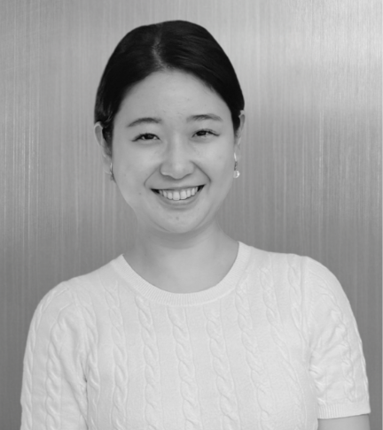 Black and white photo of a woman with dark hair smiling, wearing a white cable-knit sweater, against a plain background.