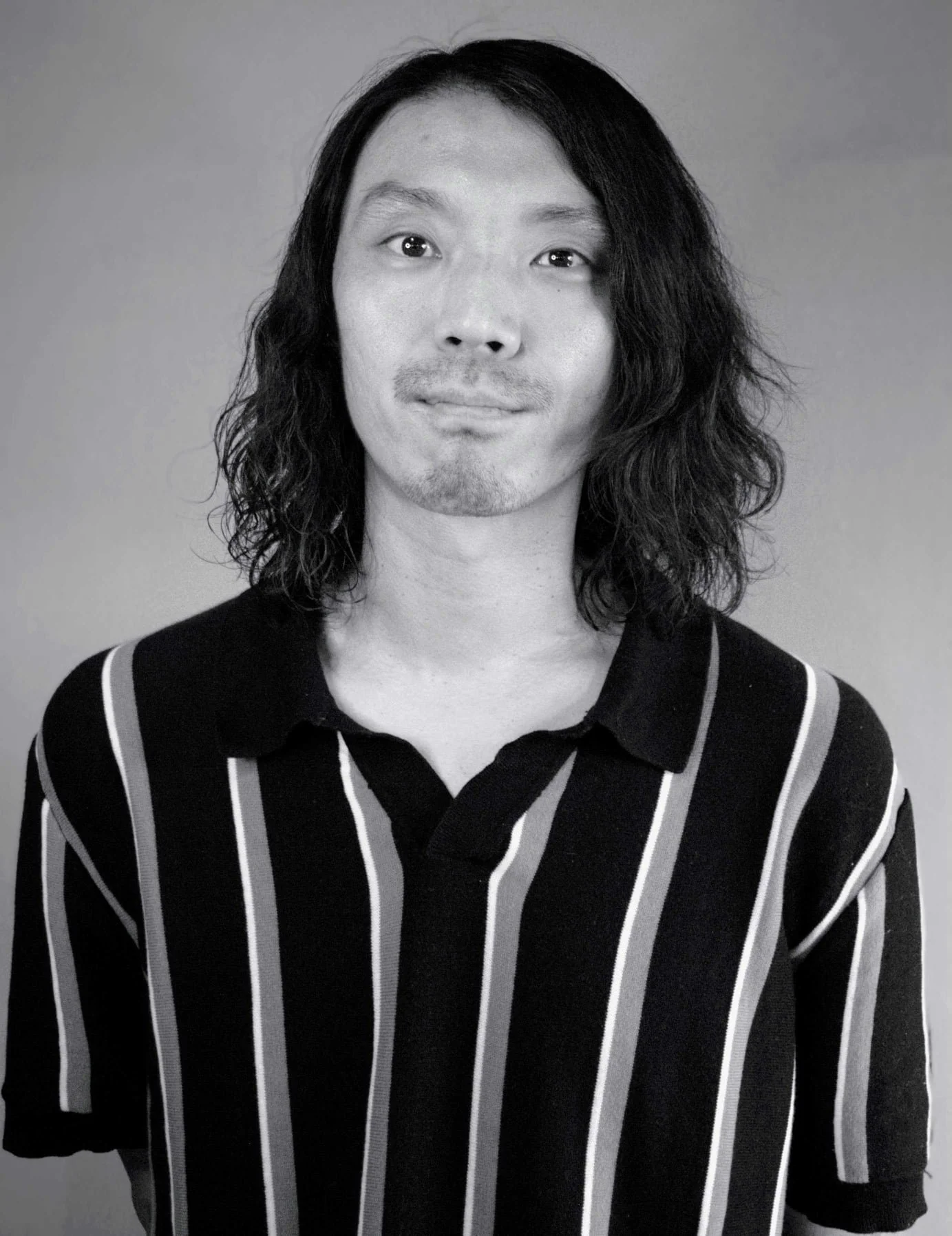 Black and white portrait of a person with long wavy hair, wearing a vertically striped shirt.