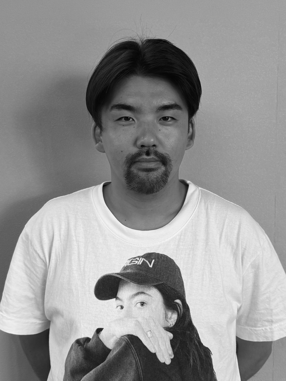 A smiling man with a beard and mustache, wearing a collared shirt, standing against a plain background in black and white.