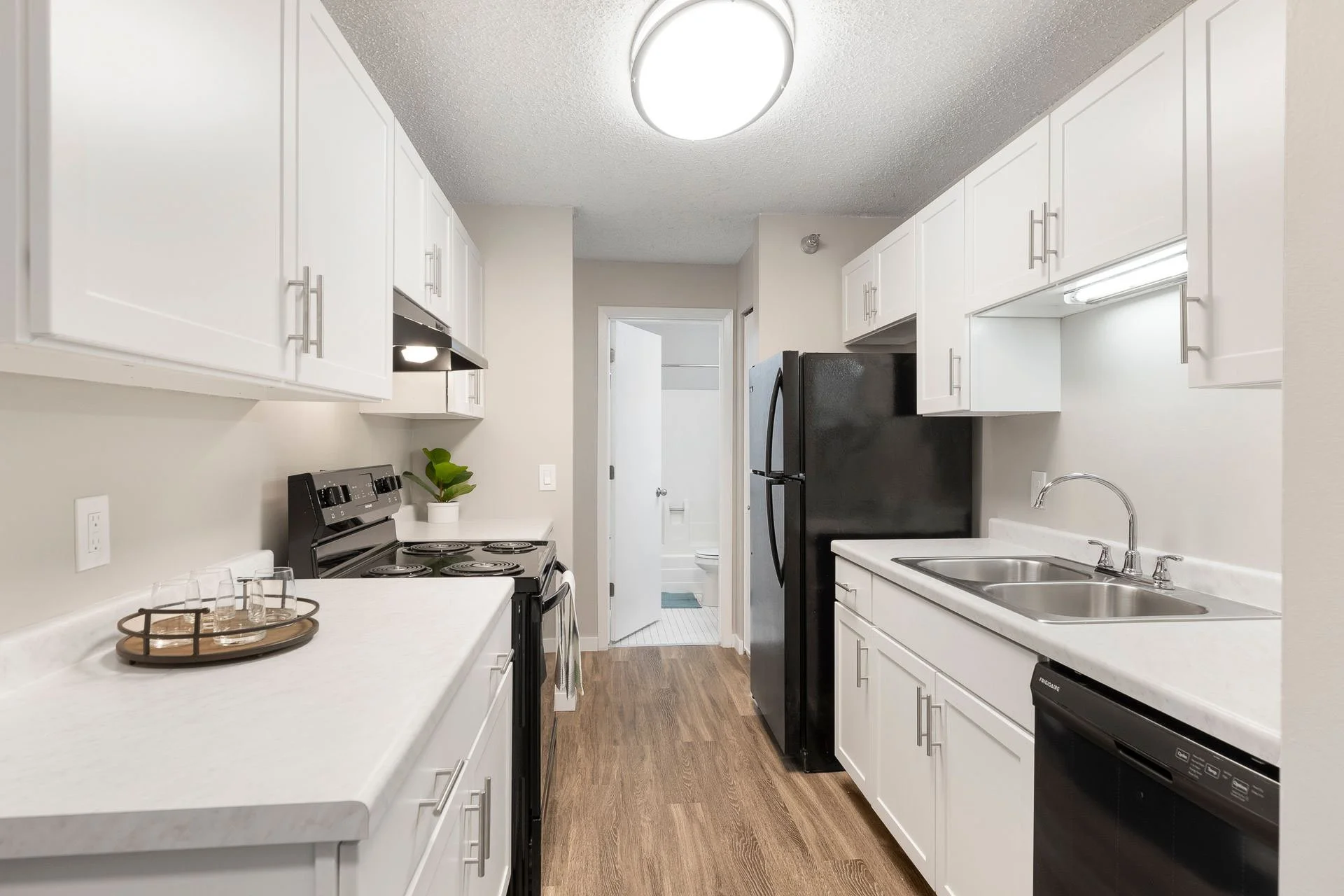 Kitchen with white cabinets, black refrigerator, white countertops, double sink, stove, and small potted plant on the counter.