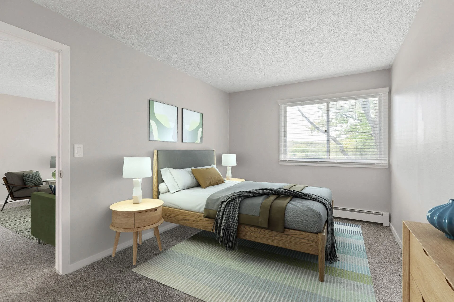 A bedroom with a bed, two nightstands with lamps, and two framed abstract art pieces on the wall. The room has a window with blinds letting in natural light.