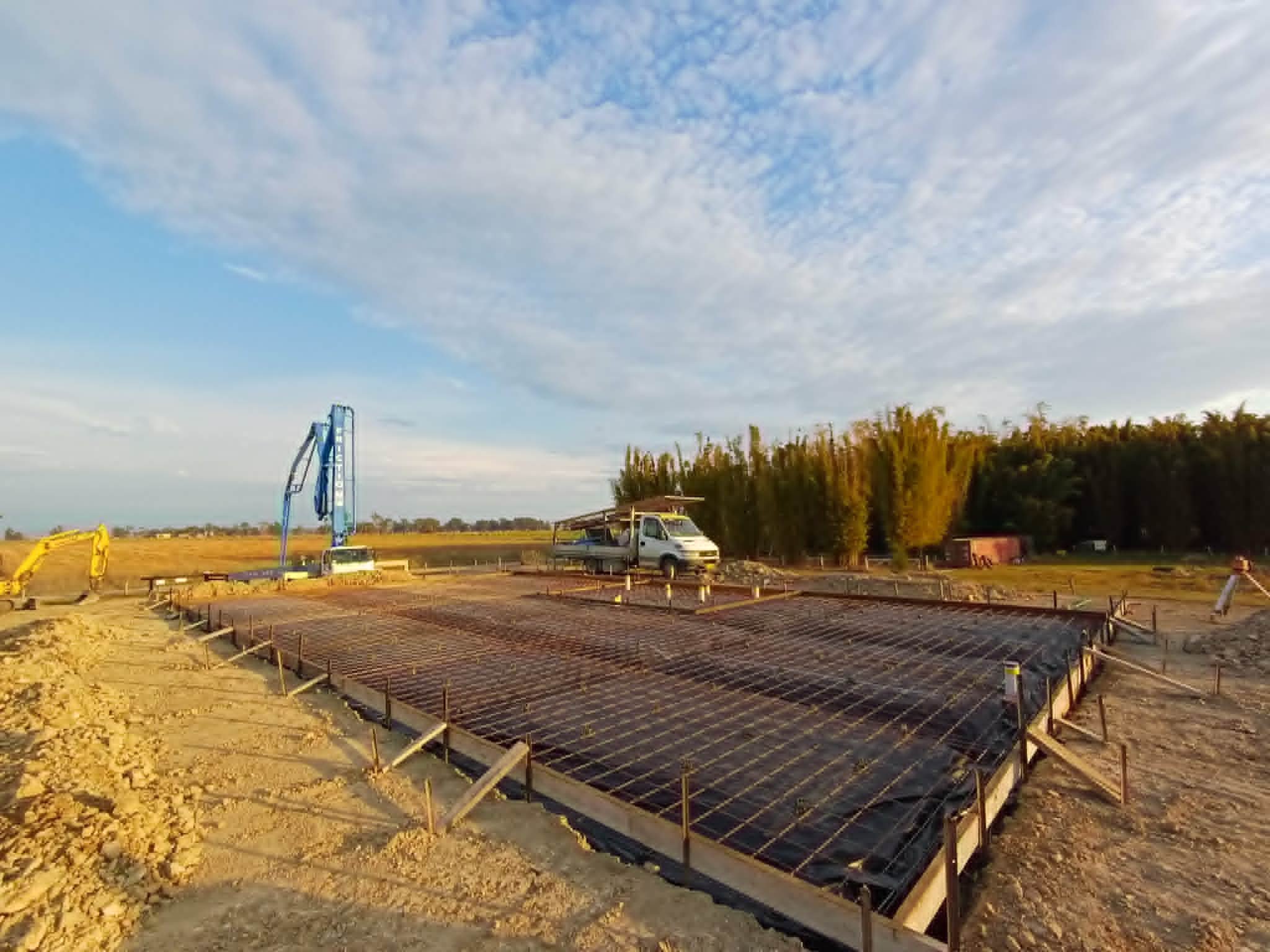 Construction site with foundation framework and construction equipment, under a partly cloudy sky.