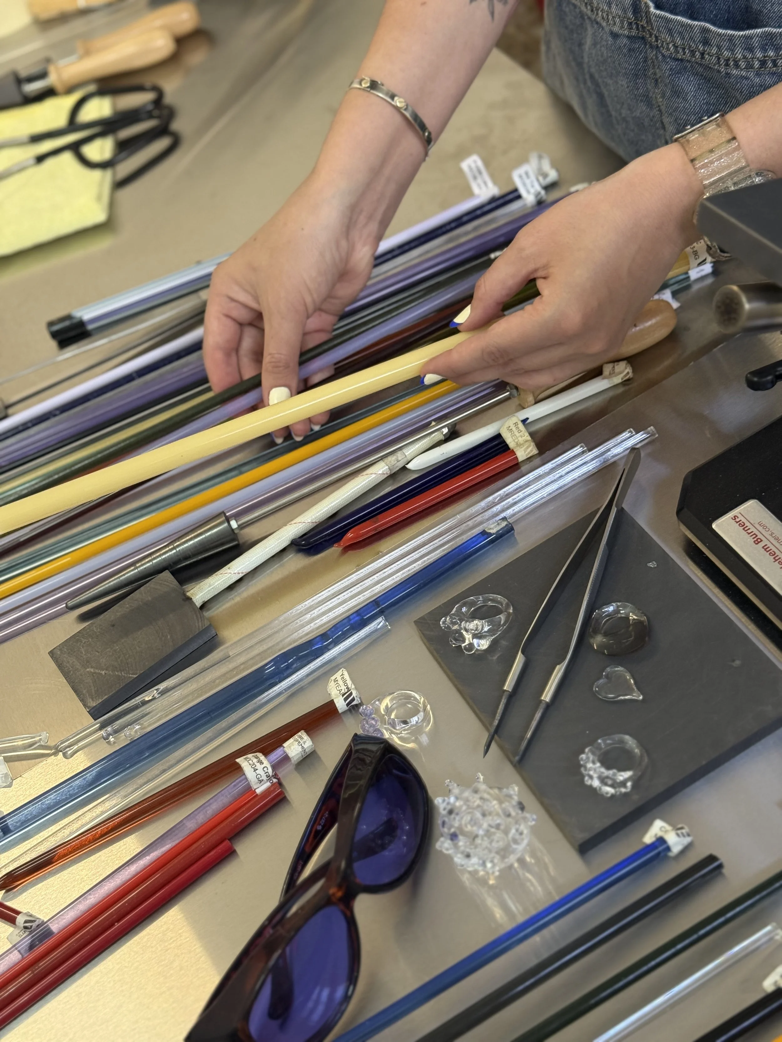 Manos arreglando varillas de acrílico y otros instrumentos en una mesa de trabajo en un taller de reparación de lentes.