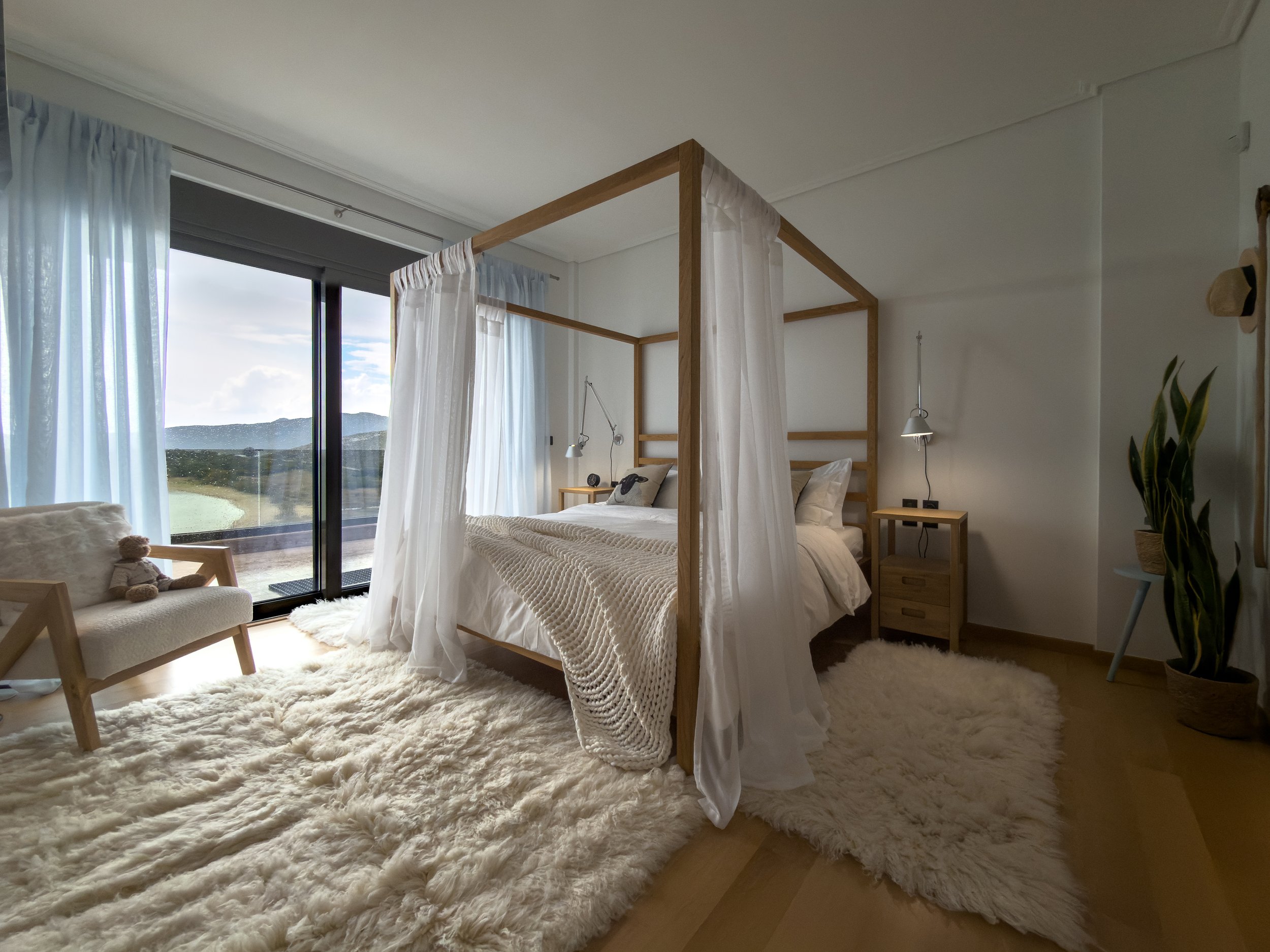 Refined bedroom interiors with canopy details, ambient softness and seamless connection to the surrounding landscape at Astraea Villa.