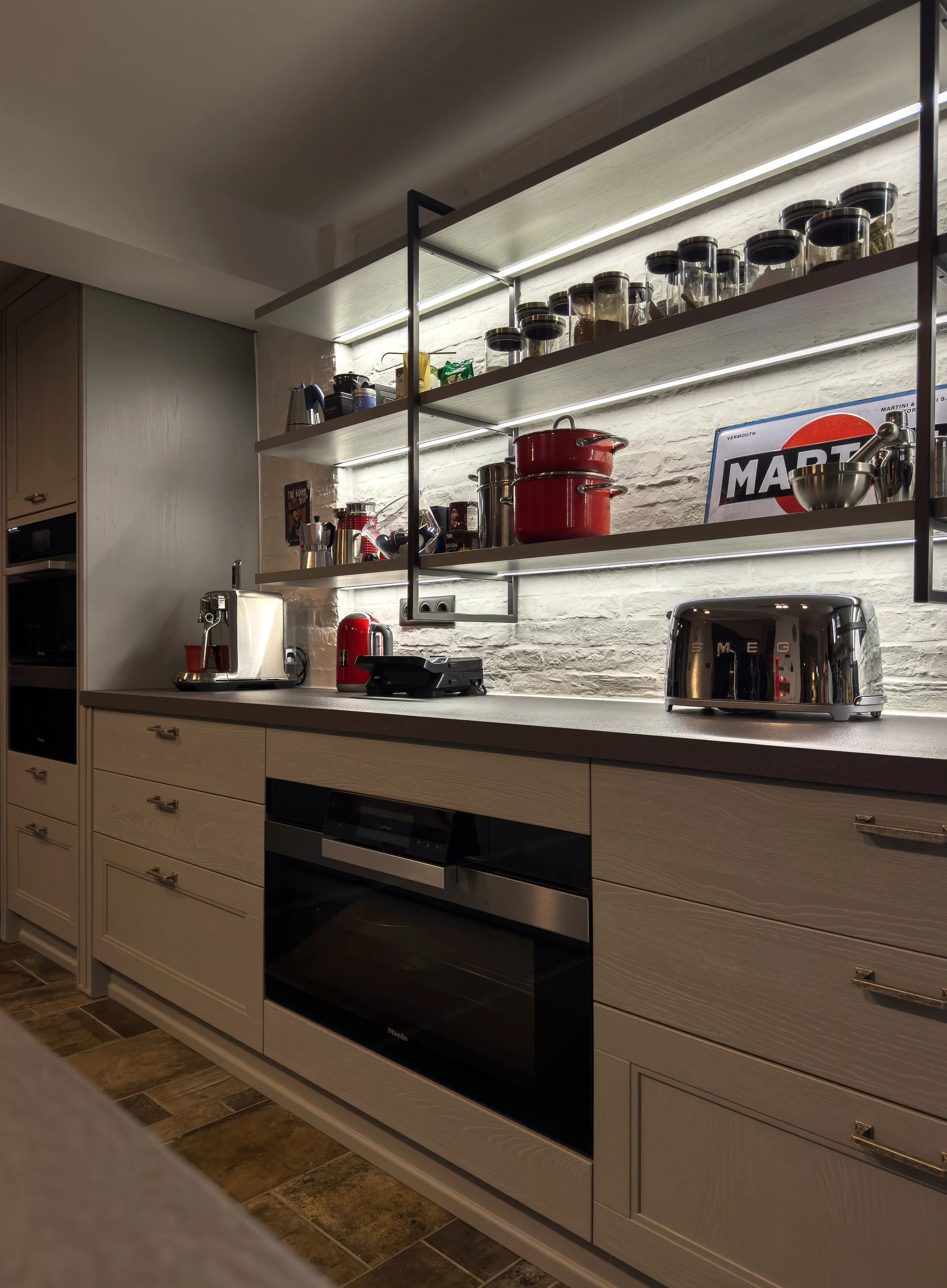 Modern kitchen with open shelving, white cabinets, black stove, toaster, red pots, and various jars and kitchenware under LED lighting.