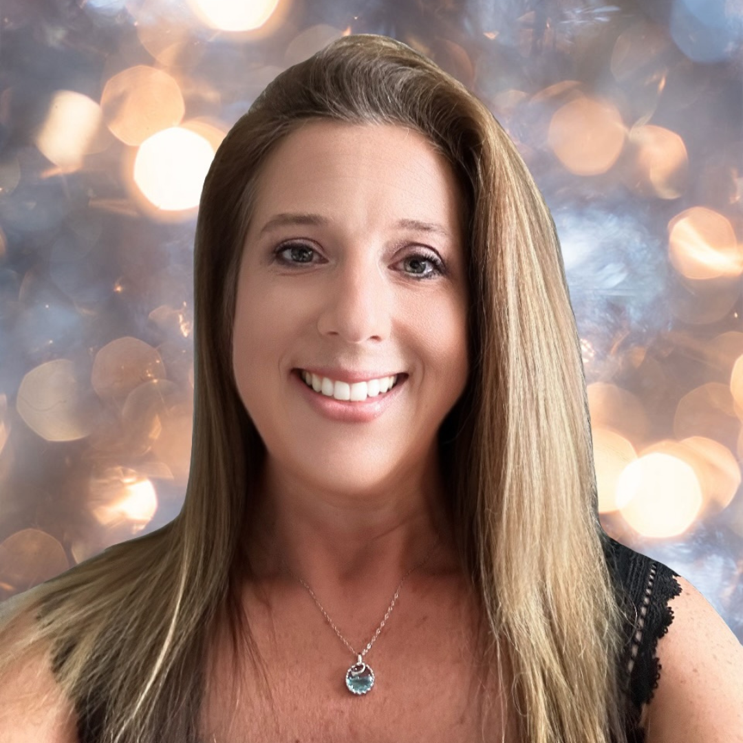 A woman with shoulder-length light brown hair, smiling, wearing a necklace and black top, against a blurred bokeh light background.