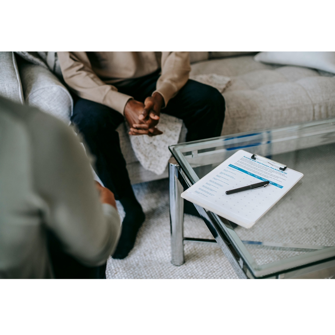 A person sitting on a sofa during a mental health assessment, with a clipboard and pen on a glass table in front of them.