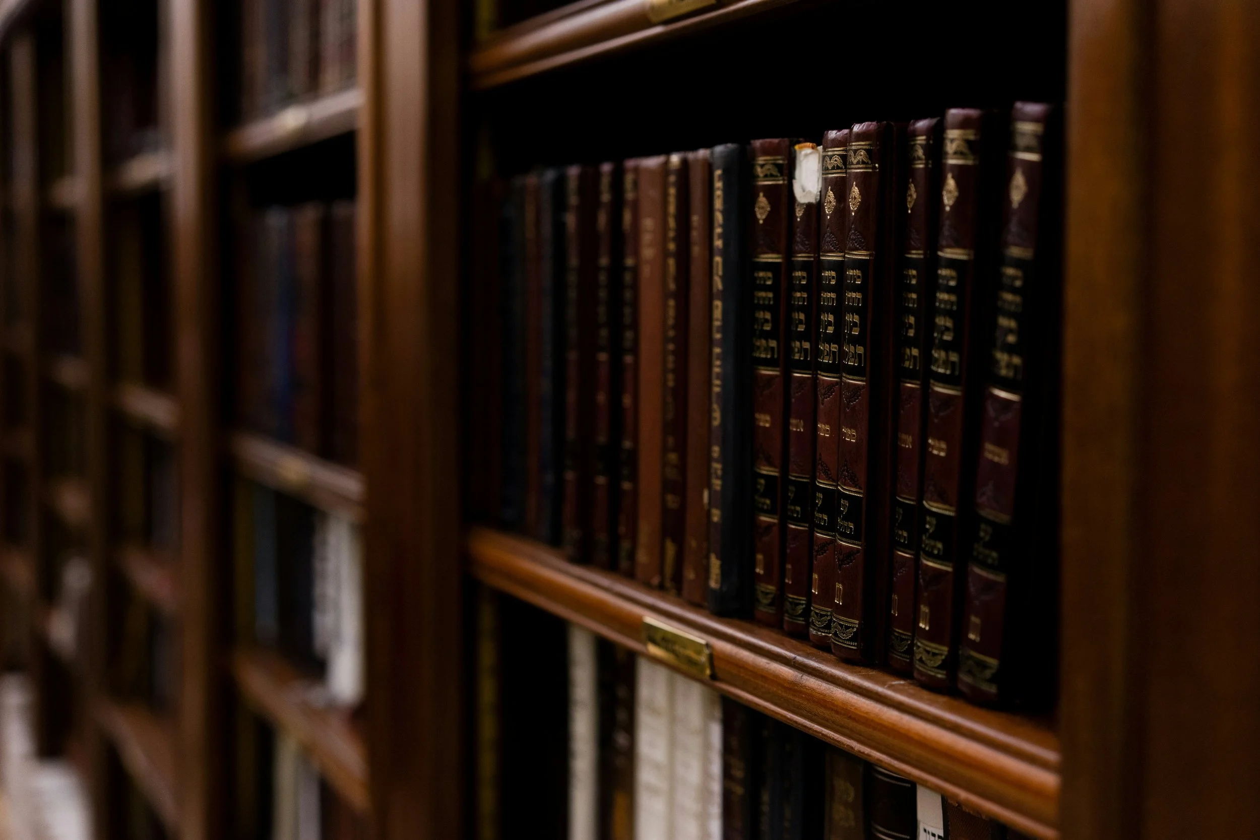 Bookshelves filled with old hardcover books, in a dimly lit library or bookstore.