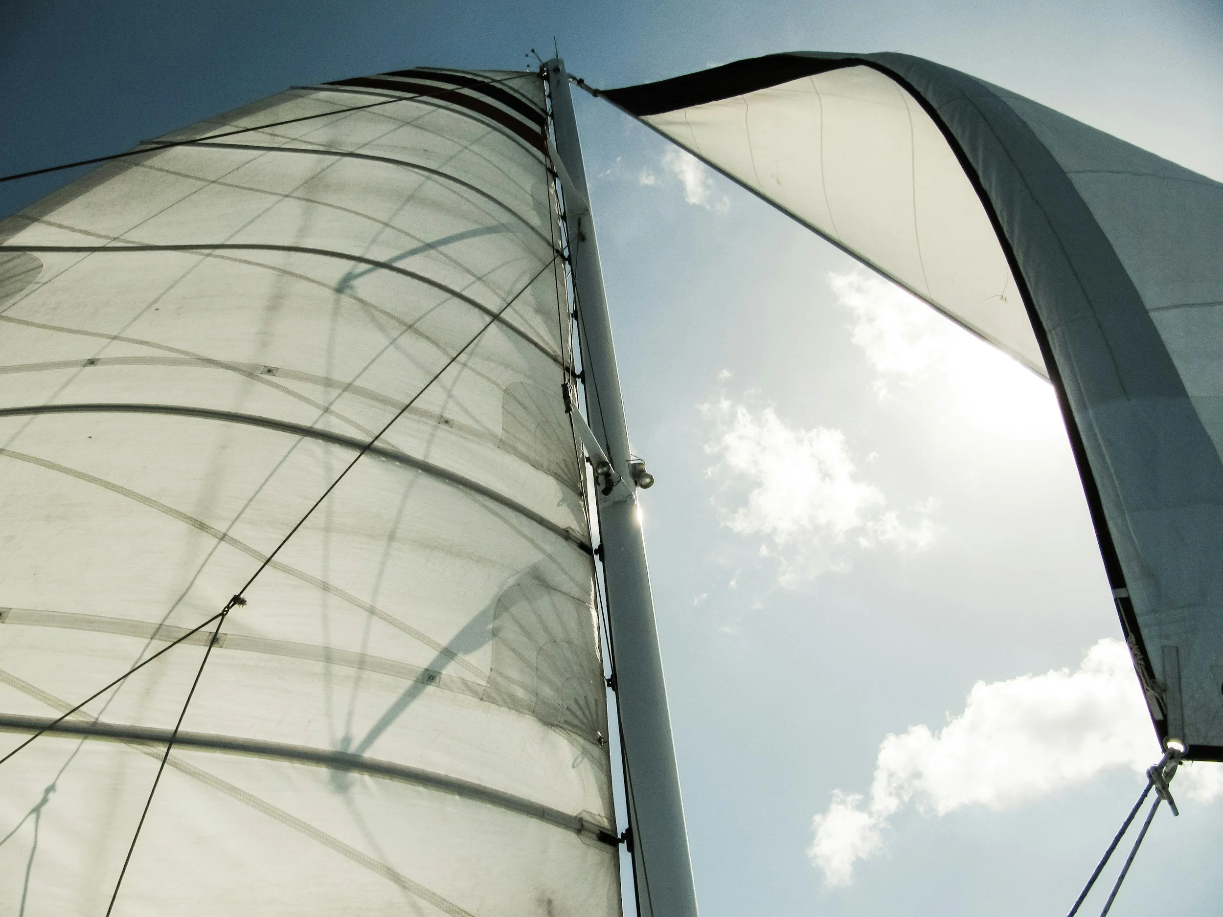 Une voile de bateau en toile blanche, vue du dessous, avec un ciel bleu en arrière-plan.