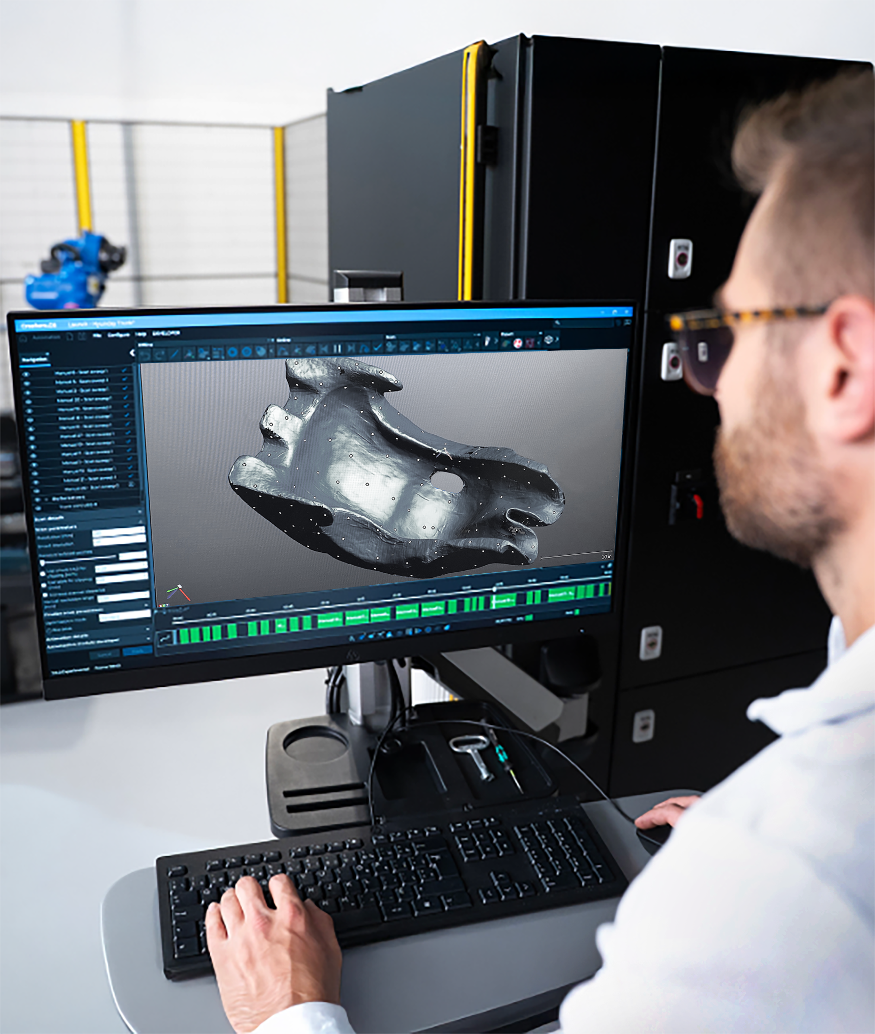 A person working on a computer with a 3D model of a racing seat displayed on the screen, in a modern workspace with technical equipment in the background.