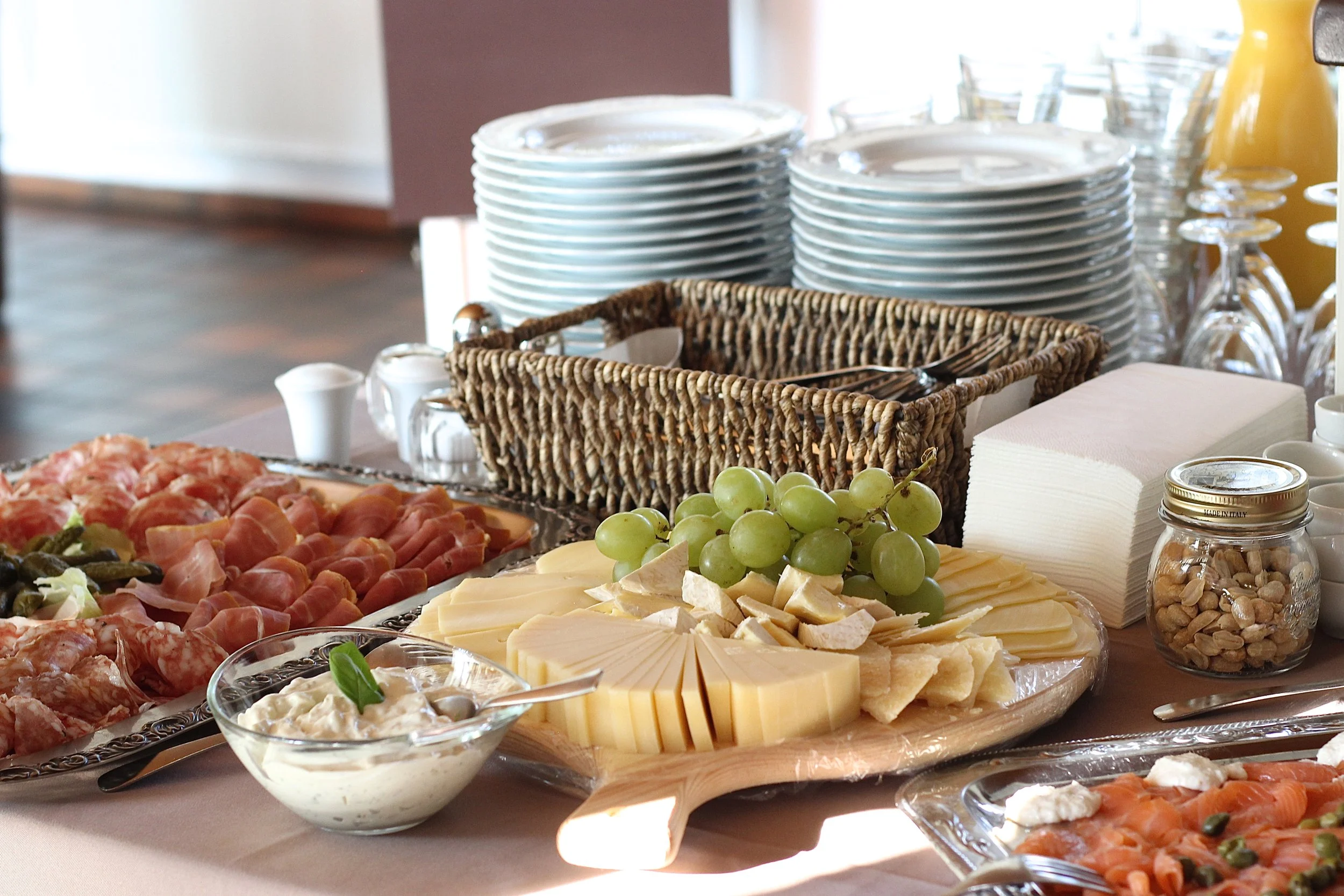 Bretter mit verschiedenen Käsesorten, Weintrauben, Wurstaufschnitt, Joghurt, Nüsse und Gläser bei einem Buffet.