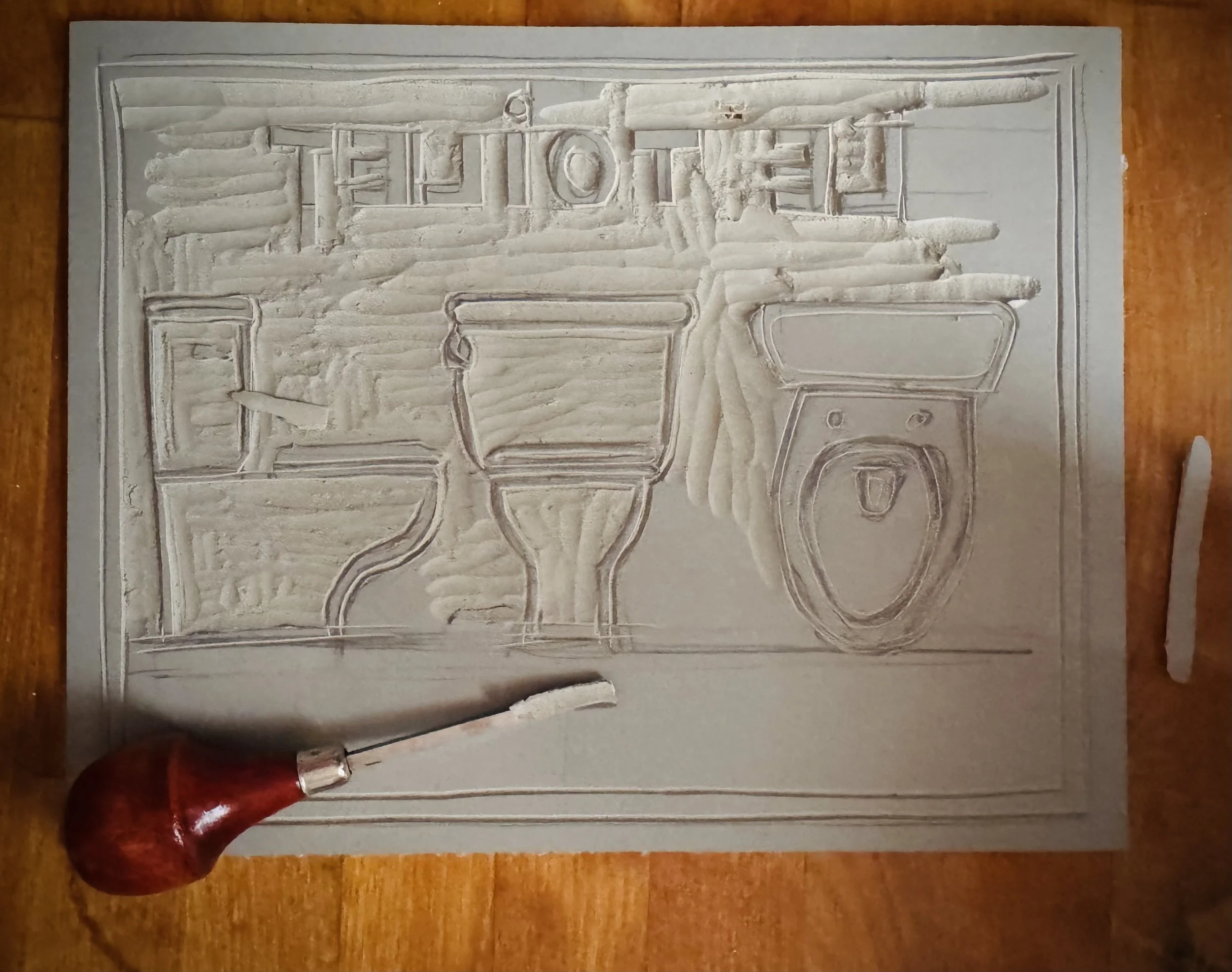 A detailed relief sculpture of a truck with various tools and objects, including a plow, a wheel, and pipes, carved into a rectangular stone plaque. A small red-handled chisel or tool is at the bottom left corner.