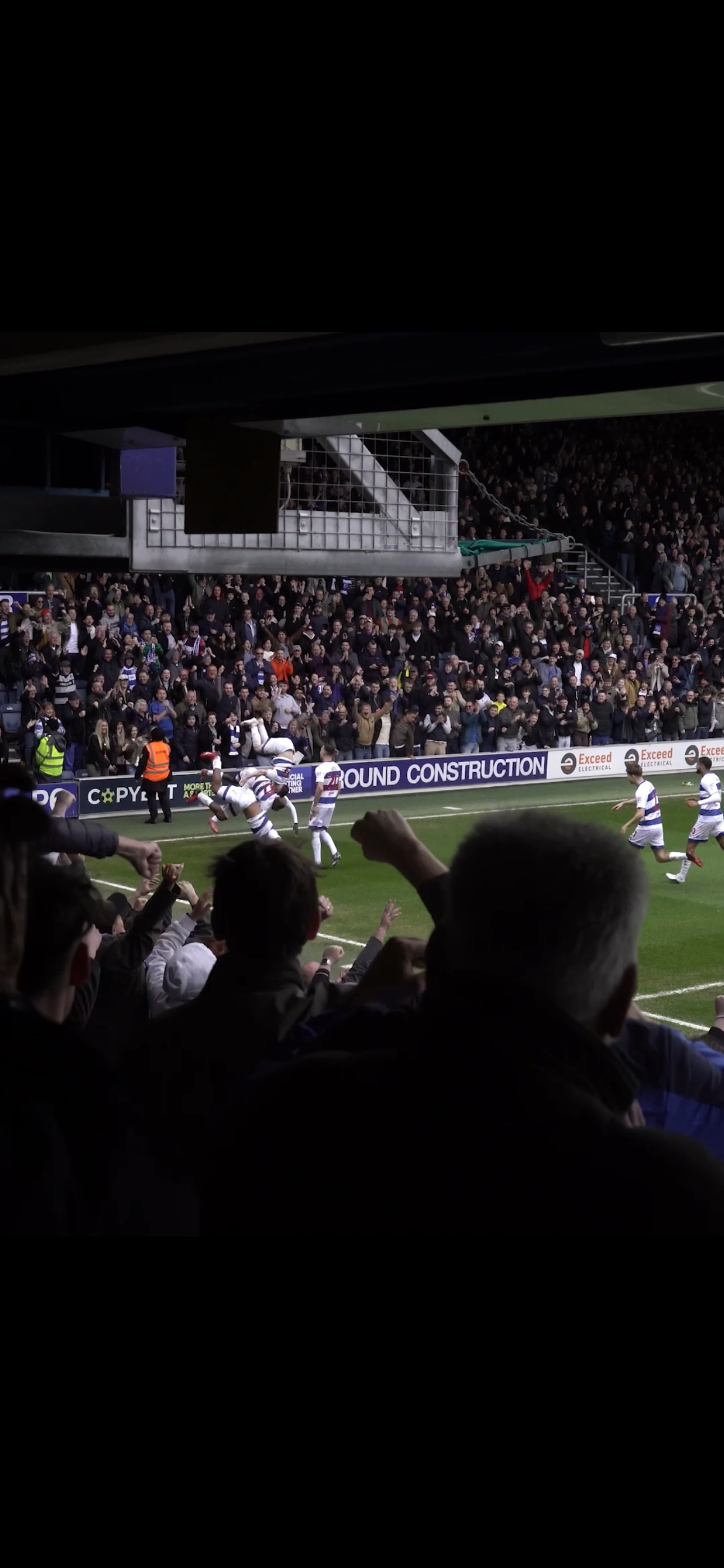 A rugby match in progress with players celebrating a try near the crowd.