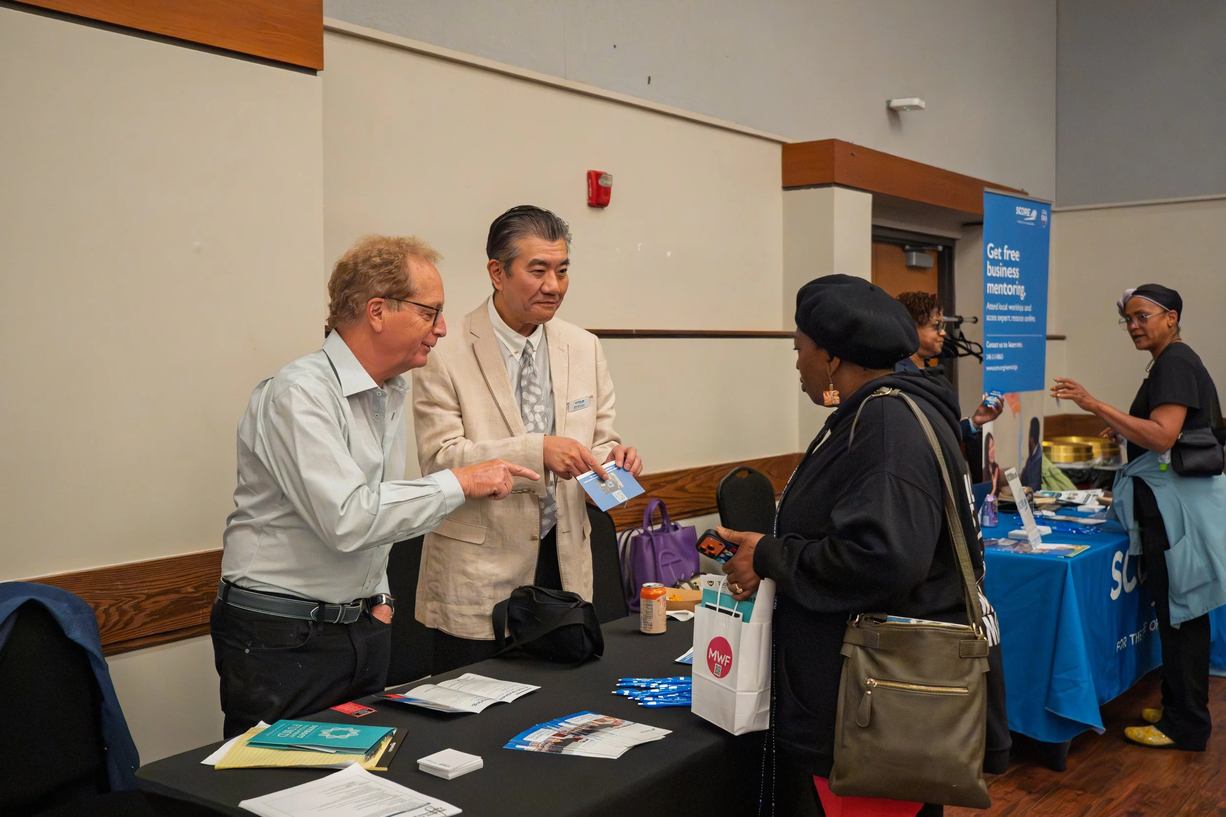 People talking at an indoor event with informational booths and banners.