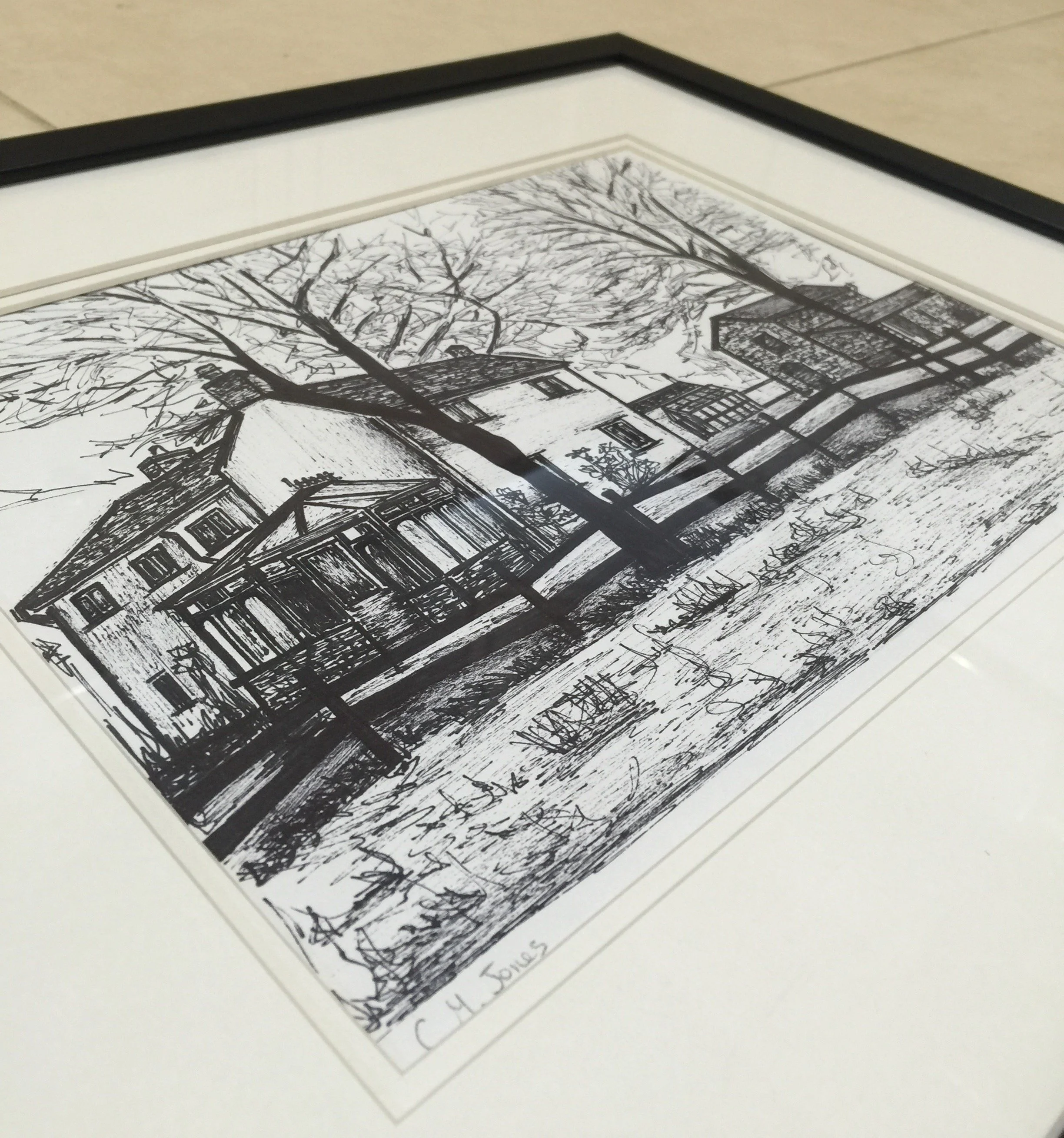 A black and white ink drawing of a house with trees surrounding it, signed and dated. The drawing is framed with a black border.