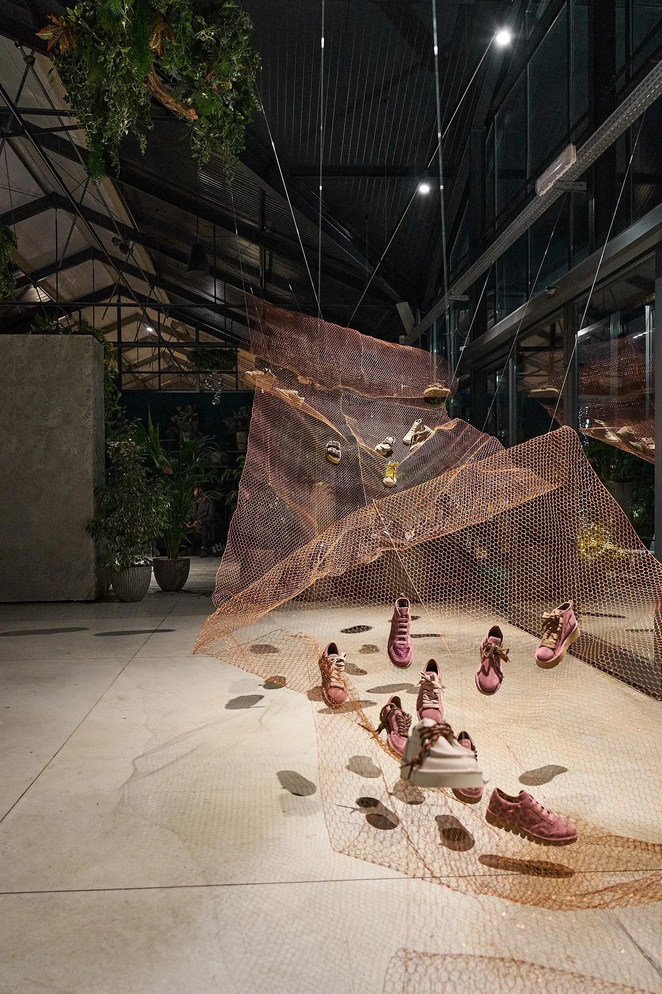 Installazione artistica con scarpe rosa e rete arancione in un ambiente moderno con piante e luci.