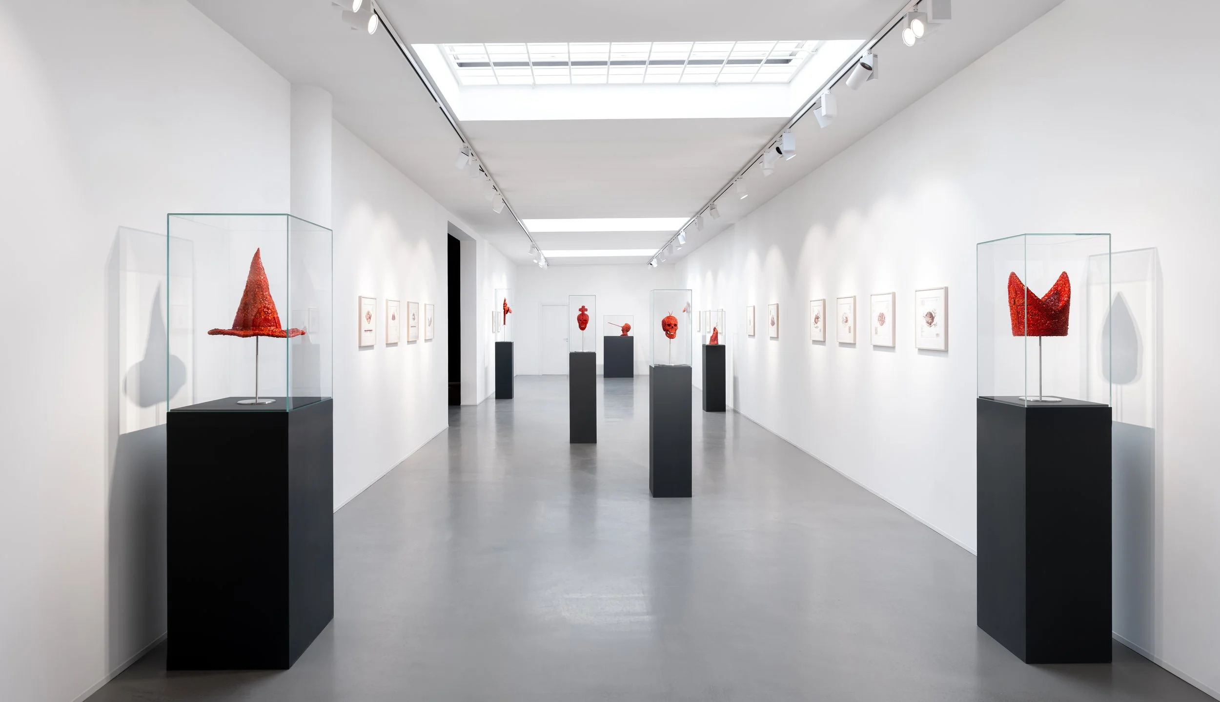 Una galleria d'arte bianca con sculture rosse esposte in teche di vetro e quadri appesi alle pareti.