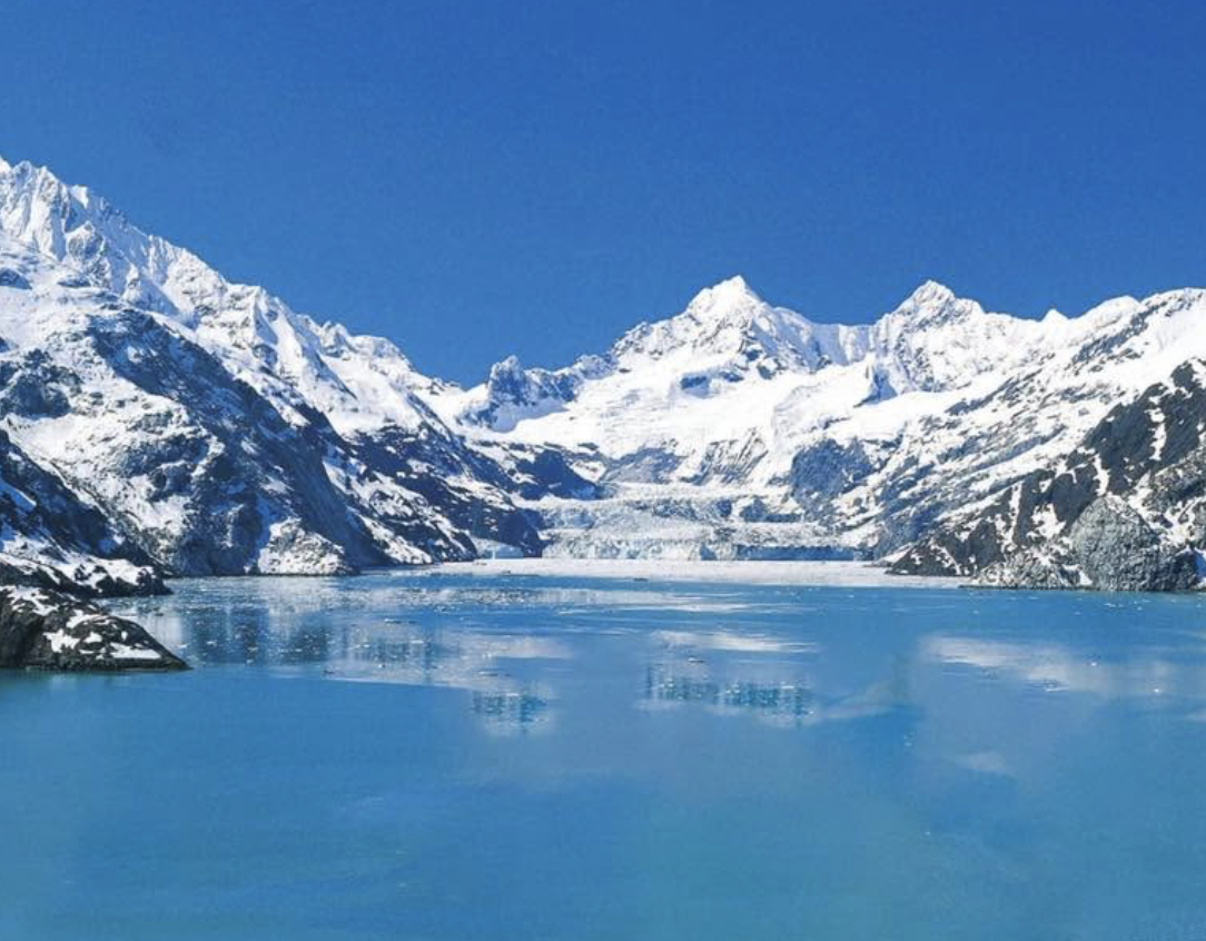 Snow-capped mountains surrounding a blue glacial lake with reflections of the mountains.