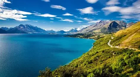 Lake with surrounding mountains and green hills under a partly cloudy sky.