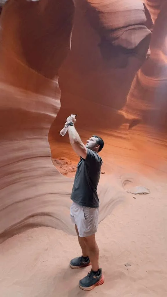 Adult man, taking photos and holding water bottle, using iPhone, in Antelope Canyon
