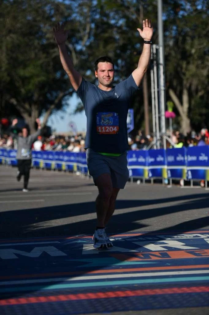 A man crossing the finish line at a race, raising his arms in celebration.