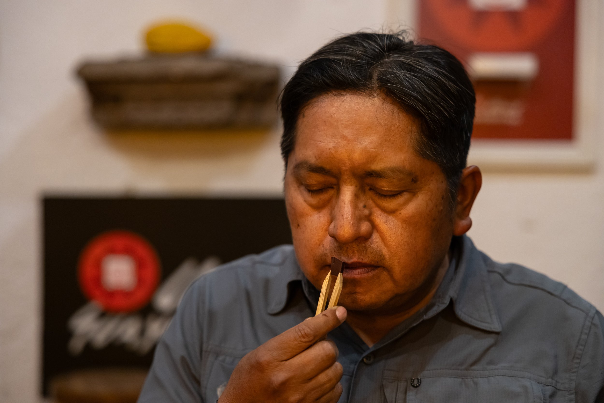 A man with black hair and tan skin is seen with his eyes closed, holding chopsticks near his mouth, as if about to eat.
