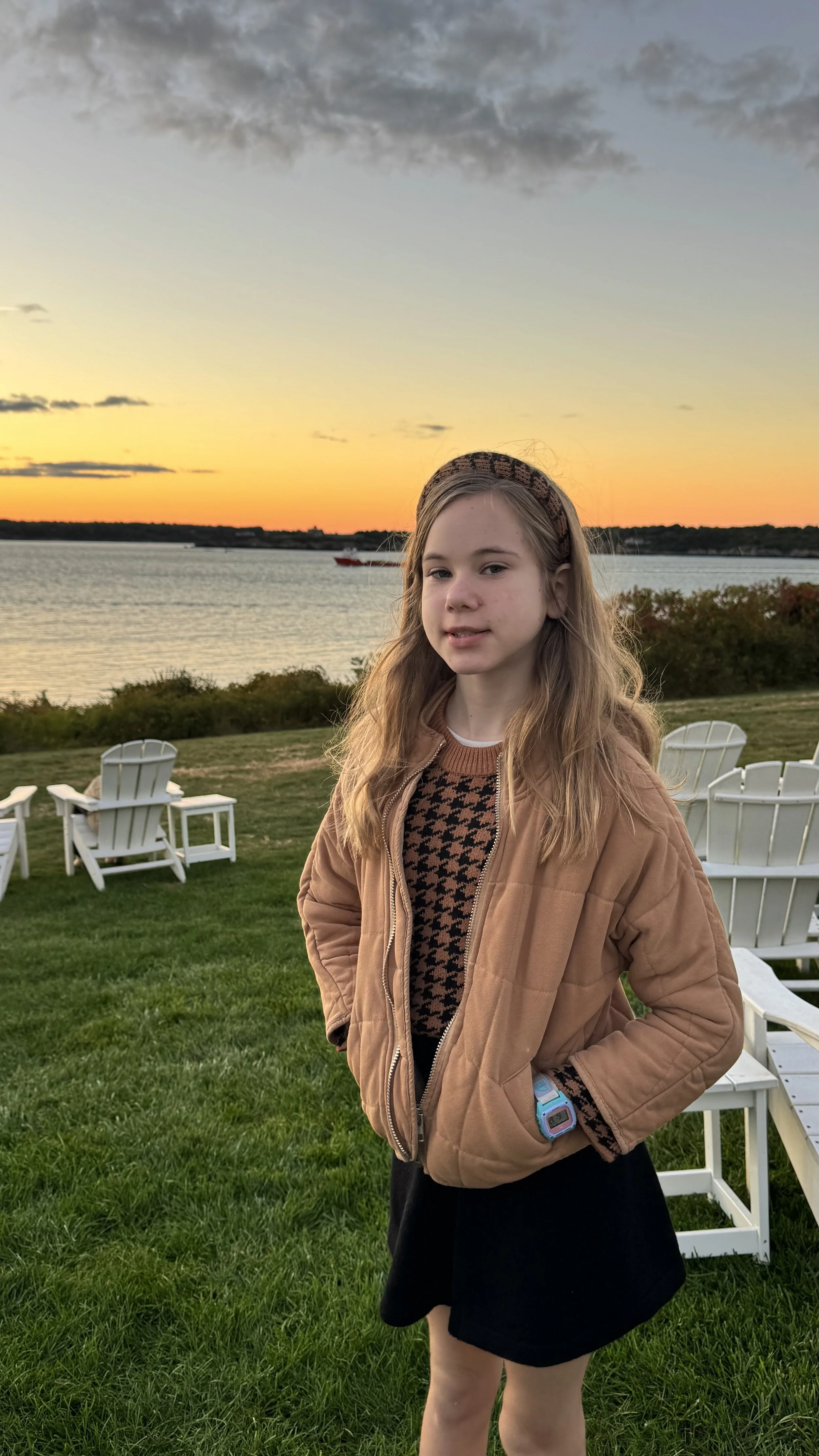 Young girl in fall, at sunset, standing in Newport, Rhode Island with Adirondack chairs in the background on the hill