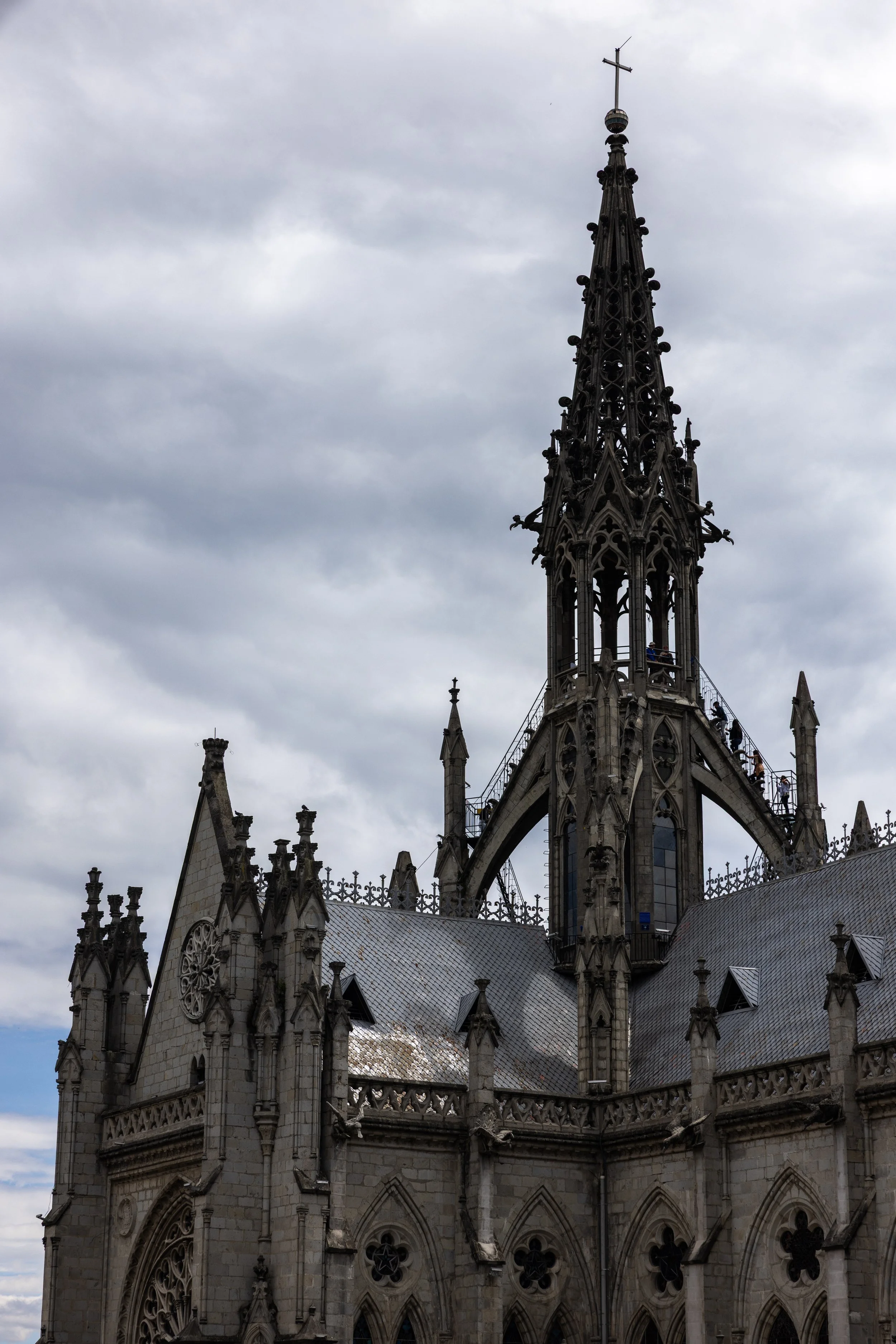 Gothic cathedral with ornate spires and a cross at the top, against a cloudy sky.