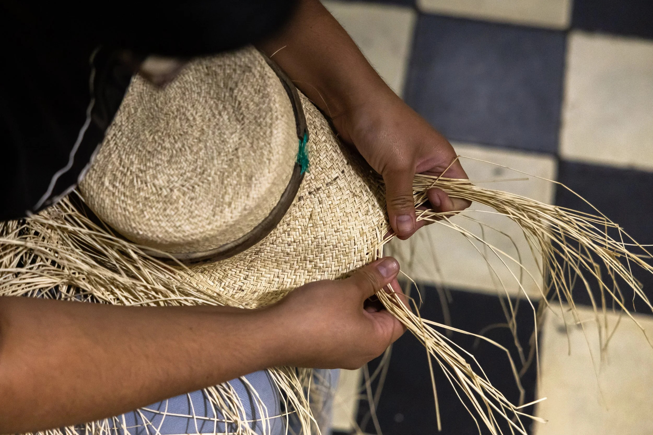 A person weaving wicker or straw material, with their hands working on a circular or rounded craft project.