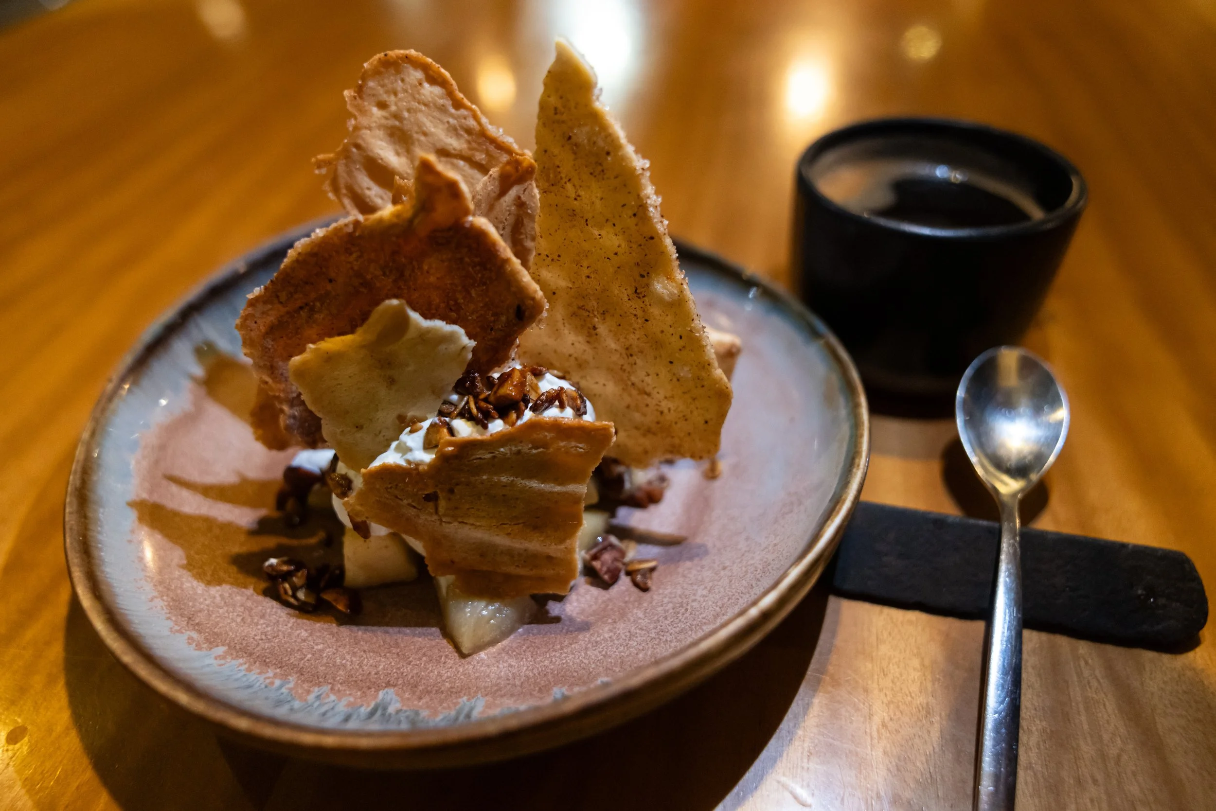 A dessert with crispy tortilla chips, whipped cream, chopped nuts, and caramel sauce in a bowl on a wooden table.