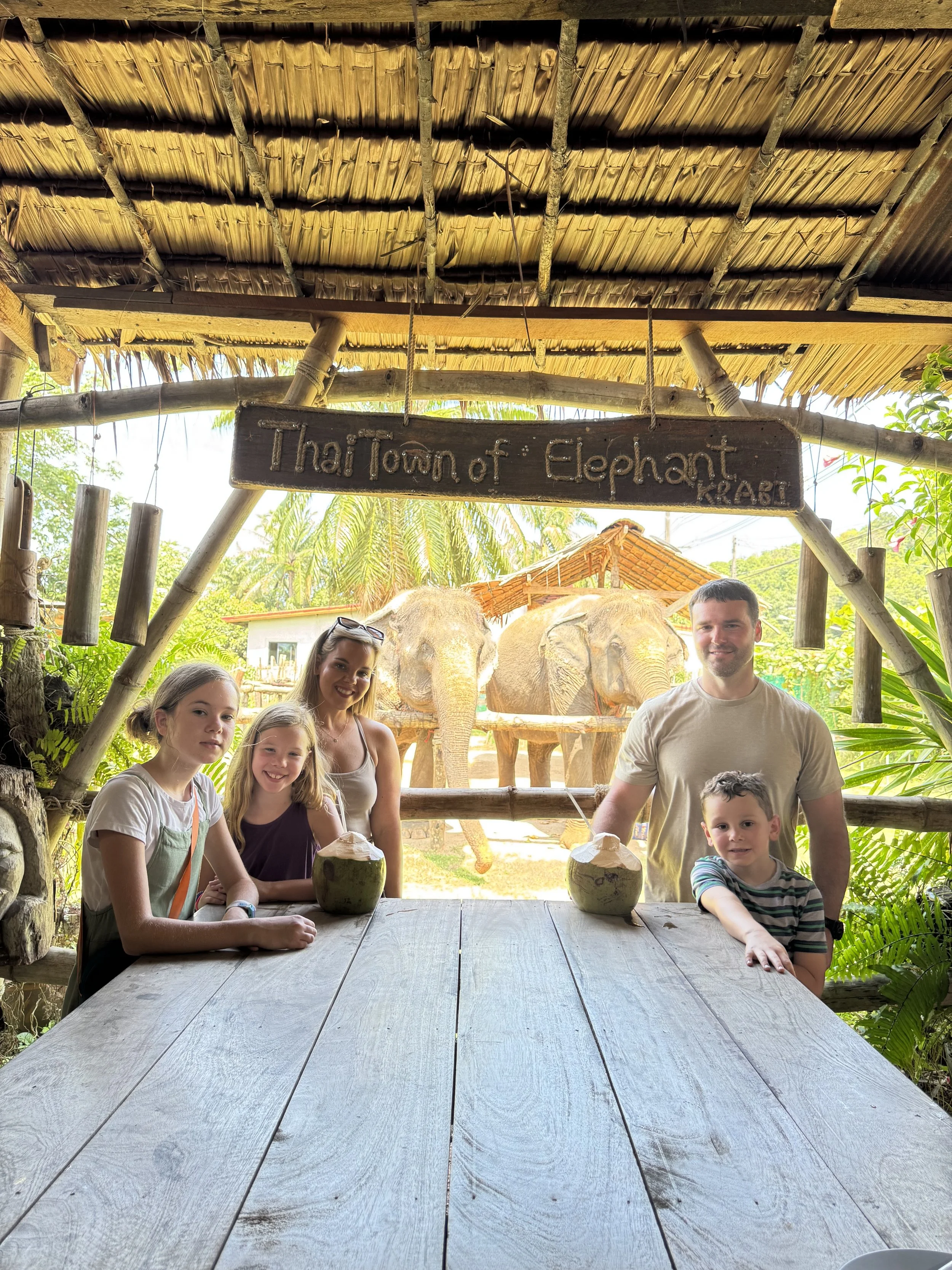 Family of 5, in Krabi Thailand at Thai Town of Elephant, drinking coconut water from coconuts with elephants in the background
