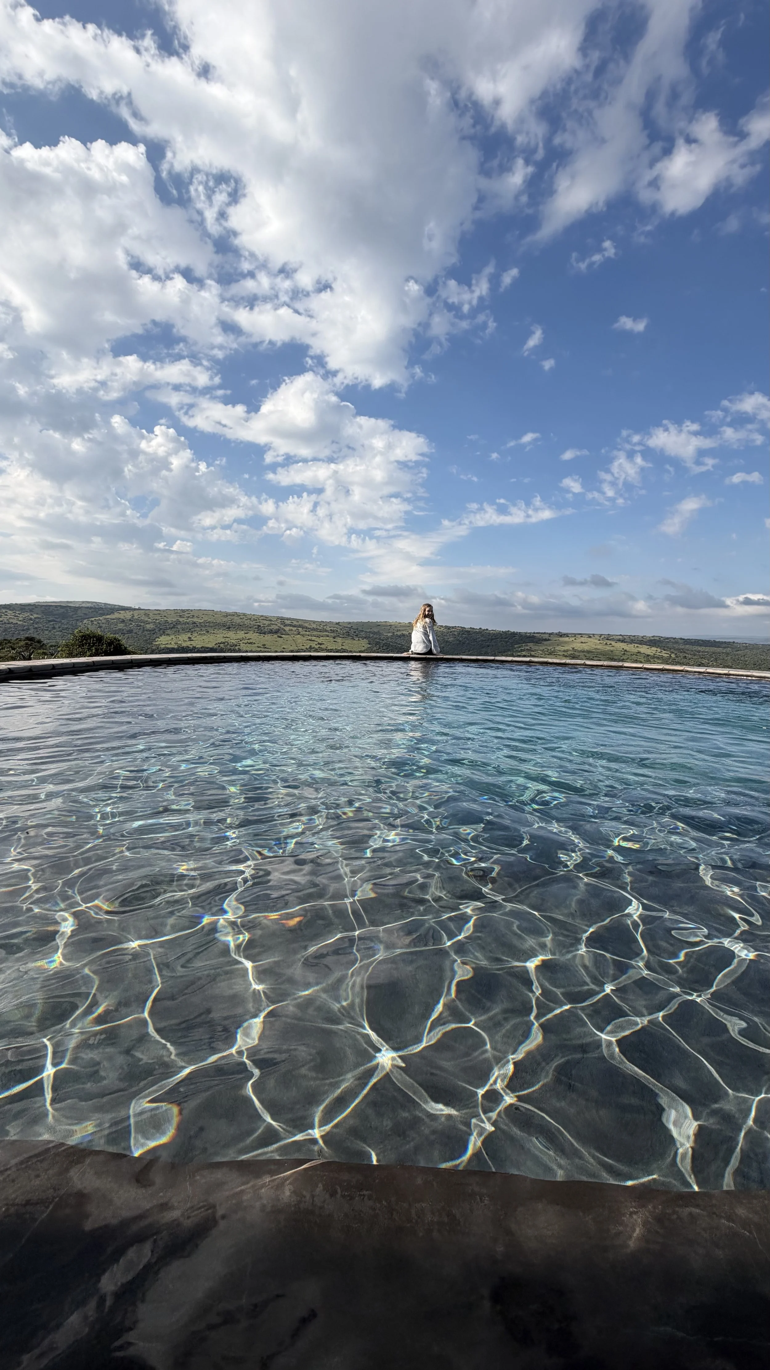 Child overlooking the safari lush green valley while sitting on the ledge of the pool