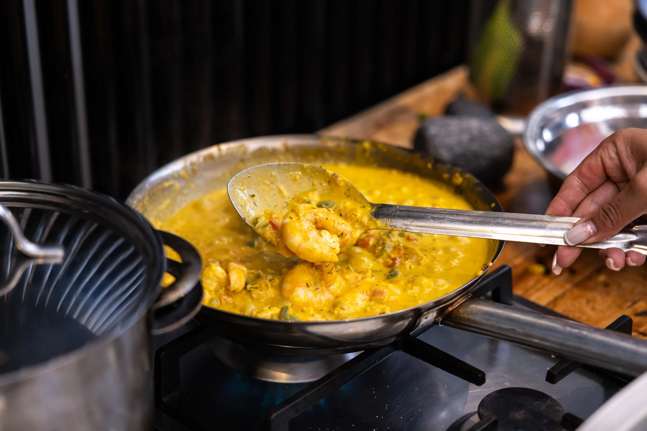 Person serving shrimp and yellow curry from large pan on stove.
