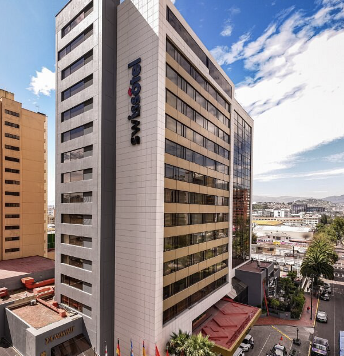 Tall modern hotel building with the name 'Swisstel' on the side, cityscape in the background, with blue sky and clouds.