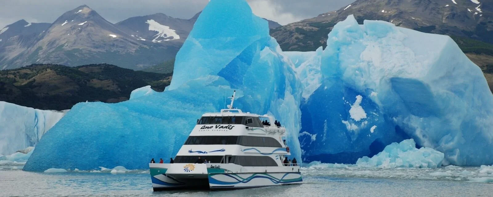 A boat sailing near large floating glaciers with mountainous terrain in the background.