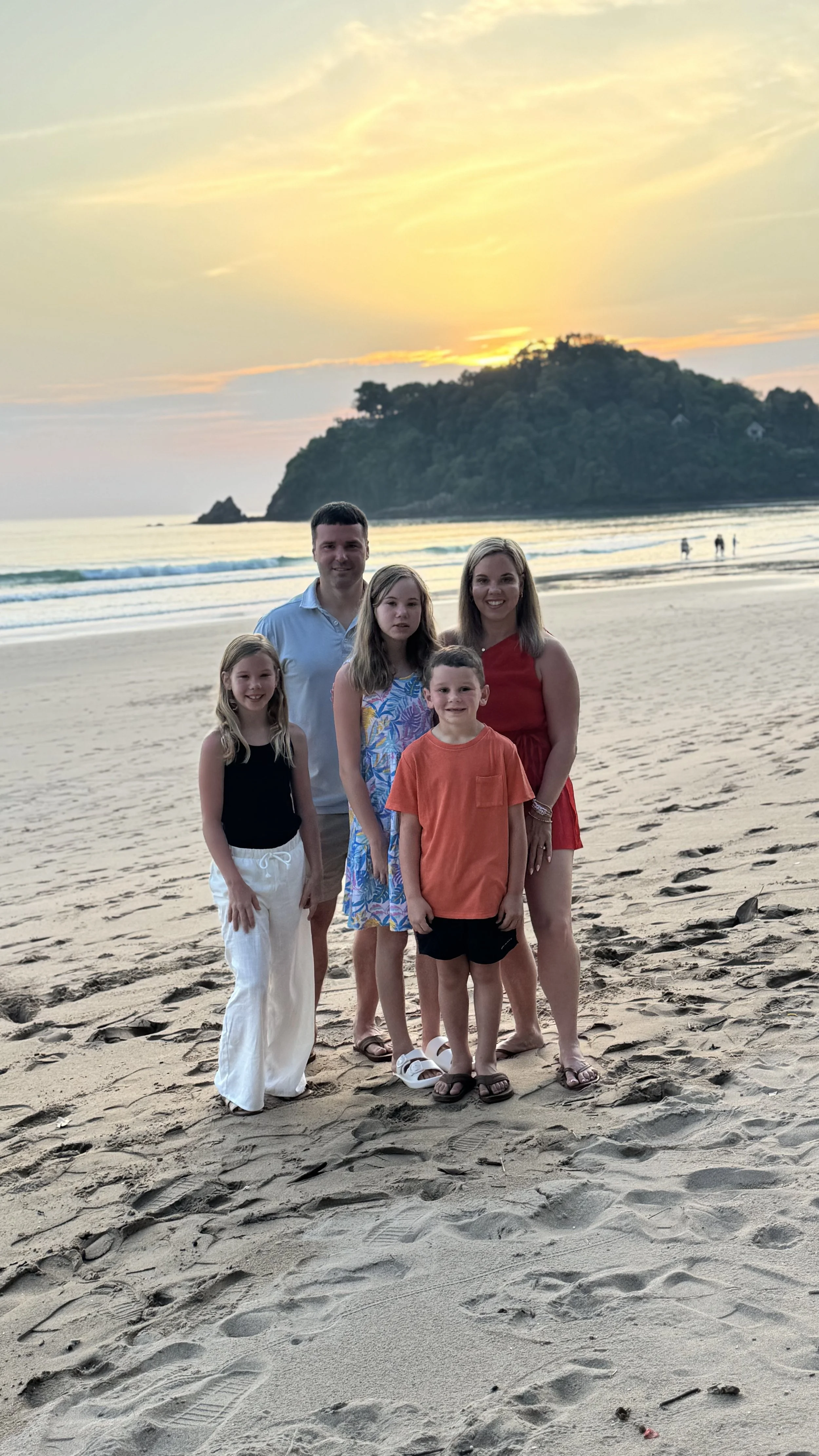 Family of 5, standing on a beach in Koh Lanta, Thailand dressed up for dinner, at sunset with mountains in the background.