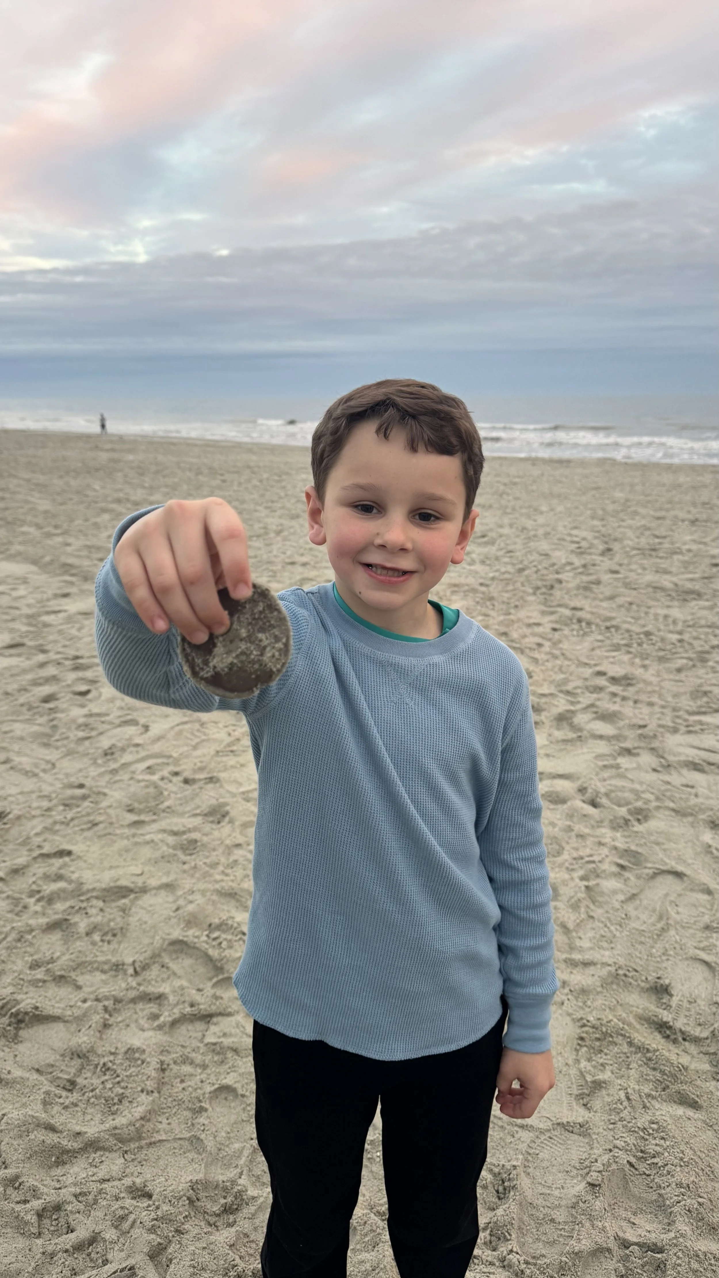 Young boy found a sand dollar on Hilton Head Island Beach with cooler temperatures for the beach trip and sunset starting in the background