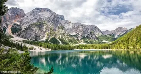 Scenic mountain landscape with a lake, surrounded by evergreen trees and rocky mountains under partly cloudy sky.