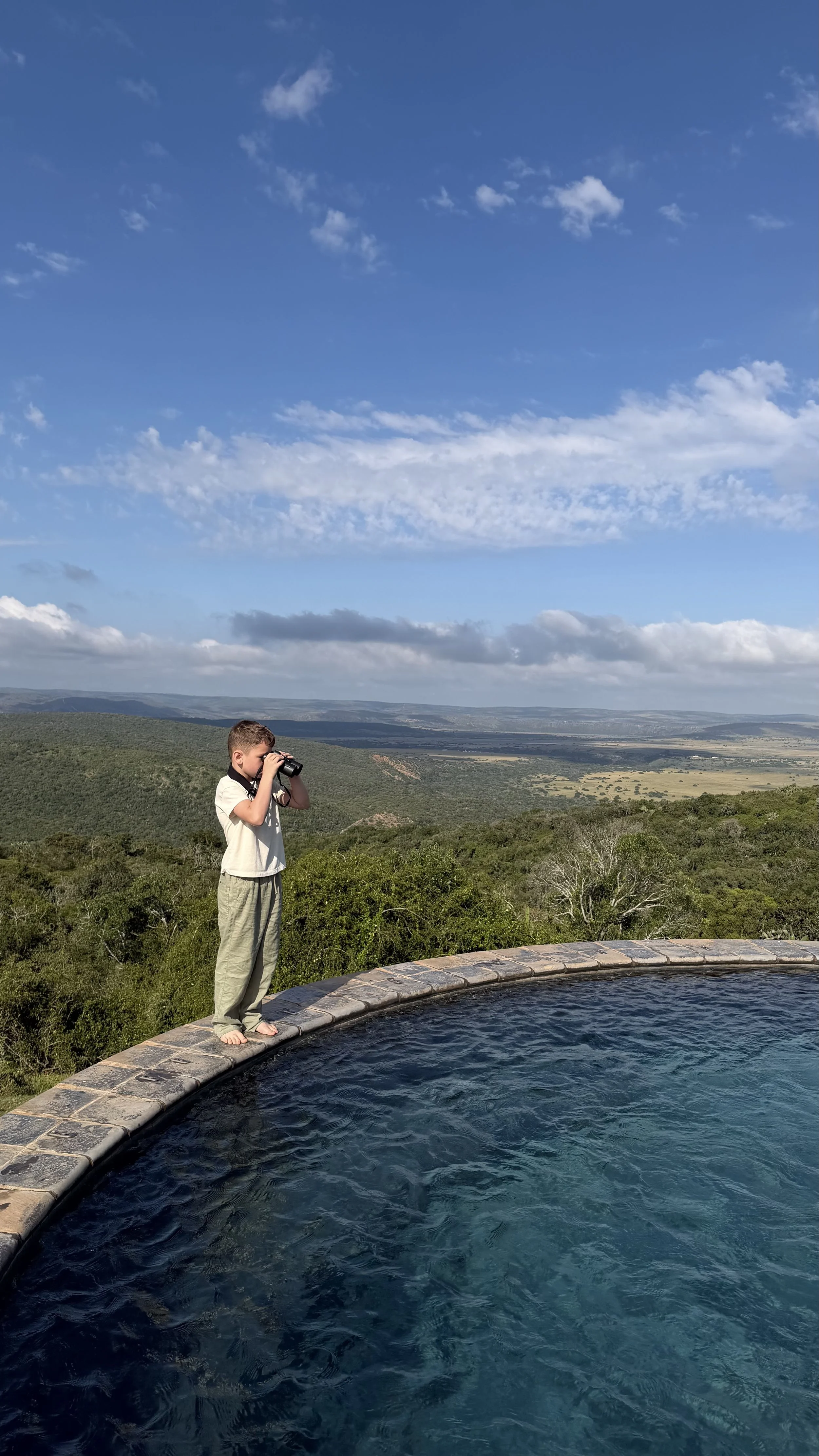 Little boy with binoculars, overlooking Founders Lodge by Mantis private game reserve, standing on a pool ledge.