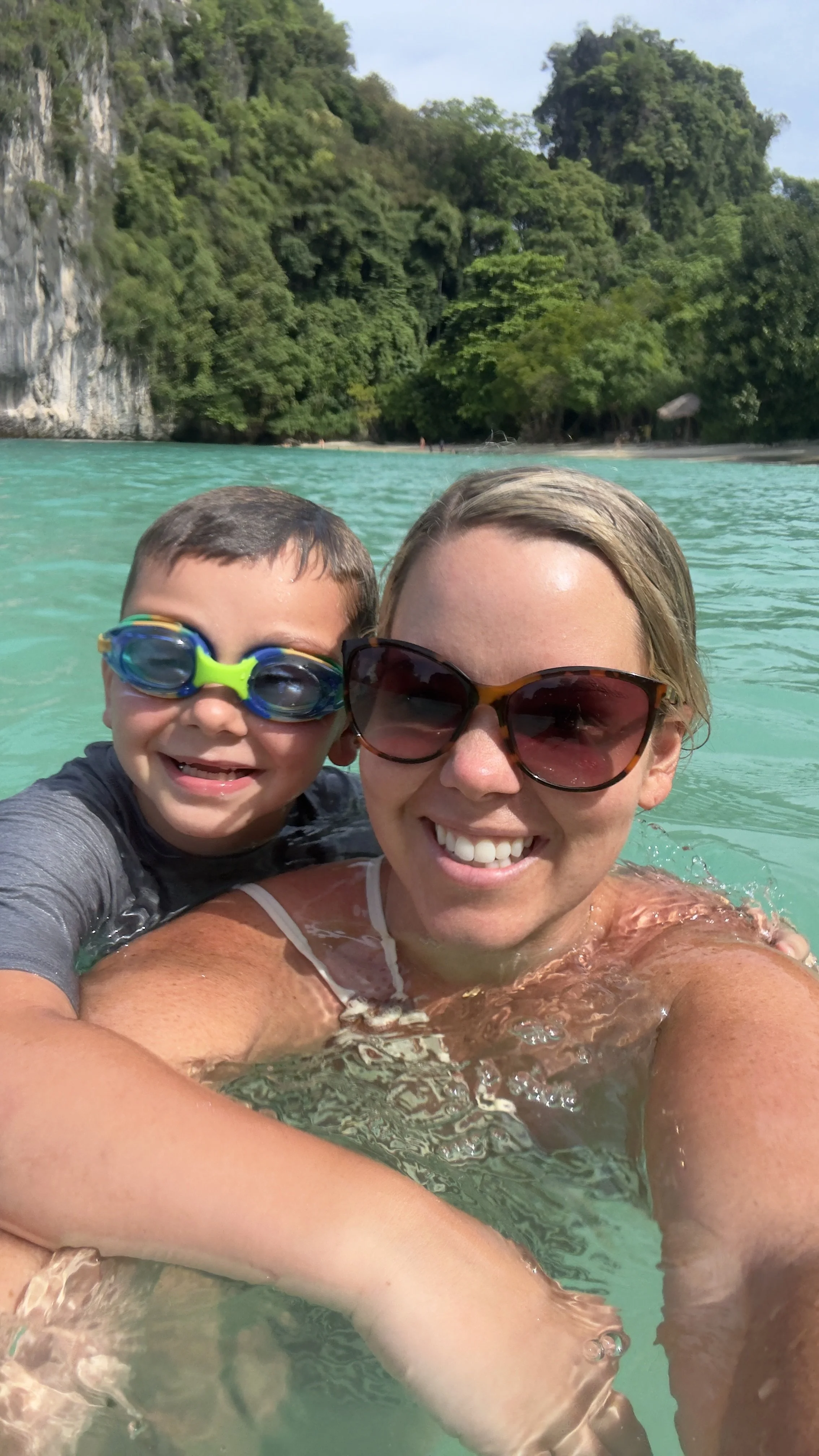 Mother and son, swimming at Hong Island in Thailand with sunglasses on and swim goggles in crystal clear water