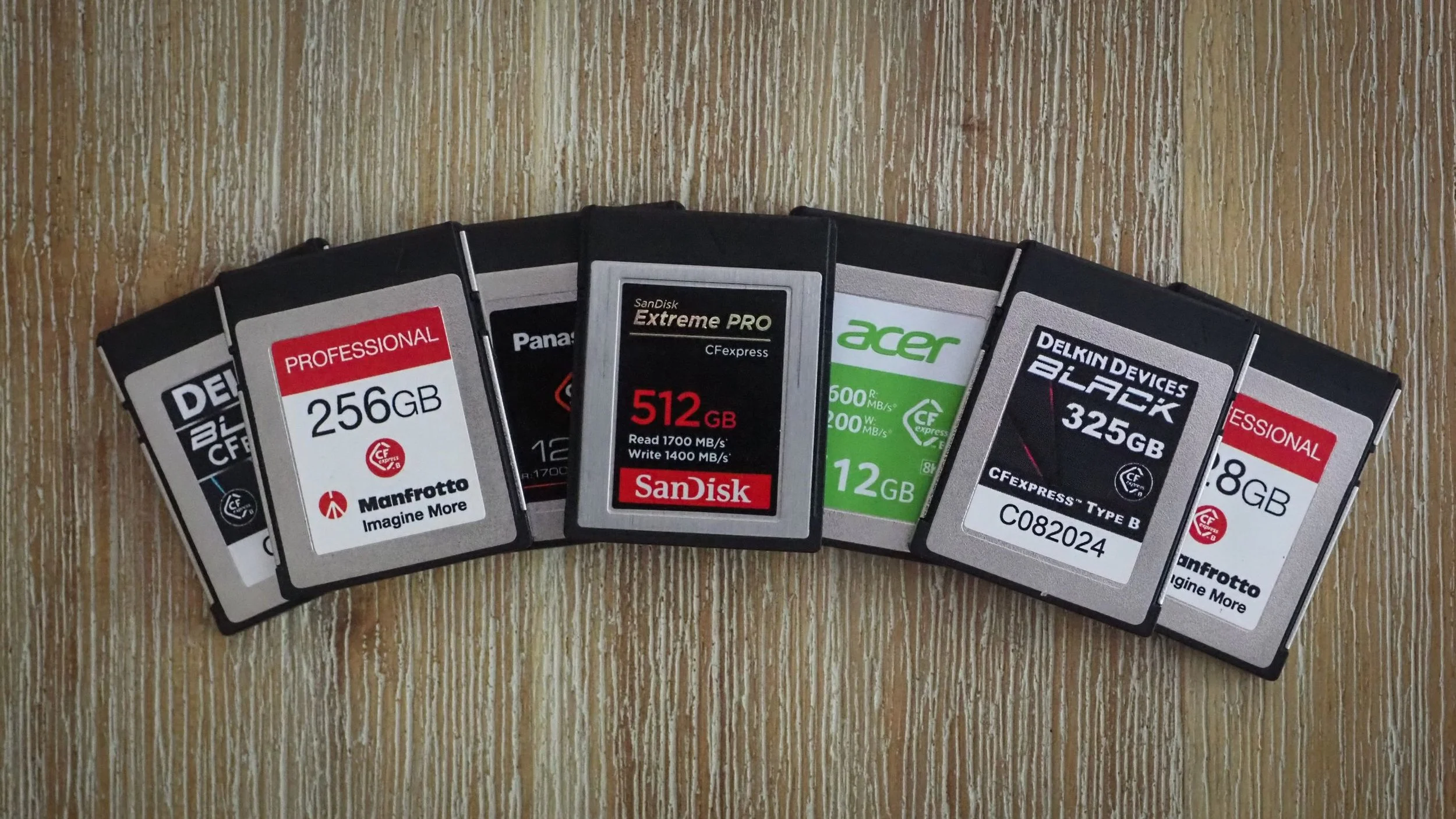 A row of various memory cards, including SanDisk, Acer, and Delkin, arranged in a curved line on a wooden surface.