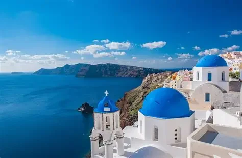 White buildings with blue domes on a cliff overlooking the ocean in Santorini, Greece.