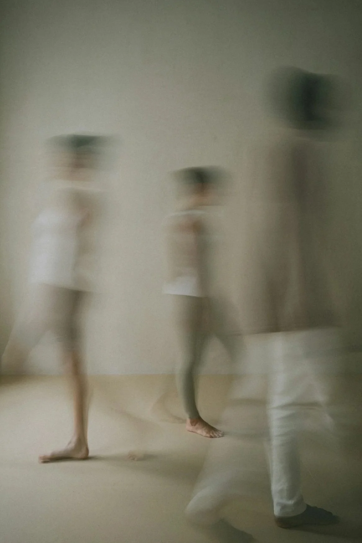 Three dancers in white costumes and black hats performing in front of a plain wall, with a blurred motion effect.