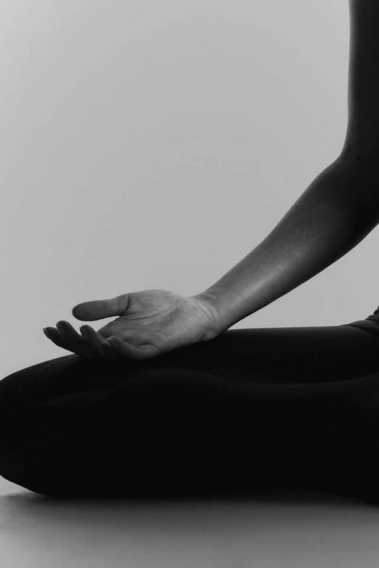 Close-up of a person performing yoga or meditation, with their hand resting on their knee, wearing dark clothing, in black and white.
