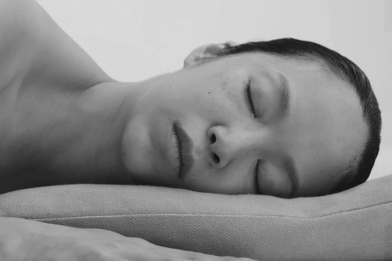 Black and white photo of a woman peacefully sleeping on a pillow with her head turned to the side.