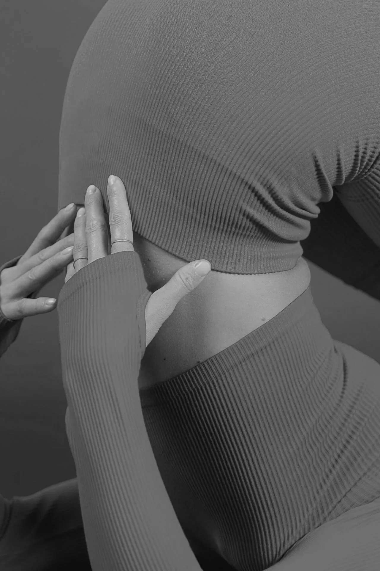 Close-up of a person wearing a textured long sleeve shirt and leggings, with hands touching their thigh.