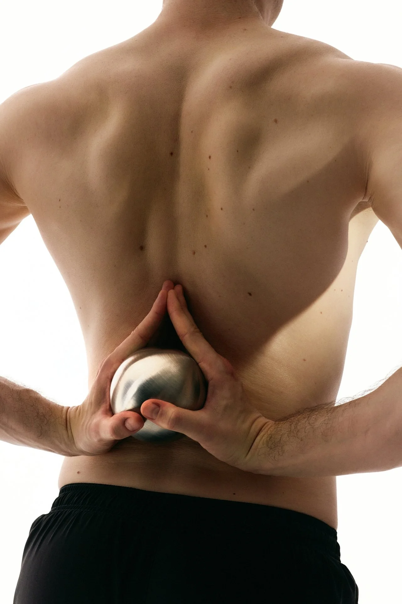 A shirtless person holding a metallic object against their lower back with another person's hand.