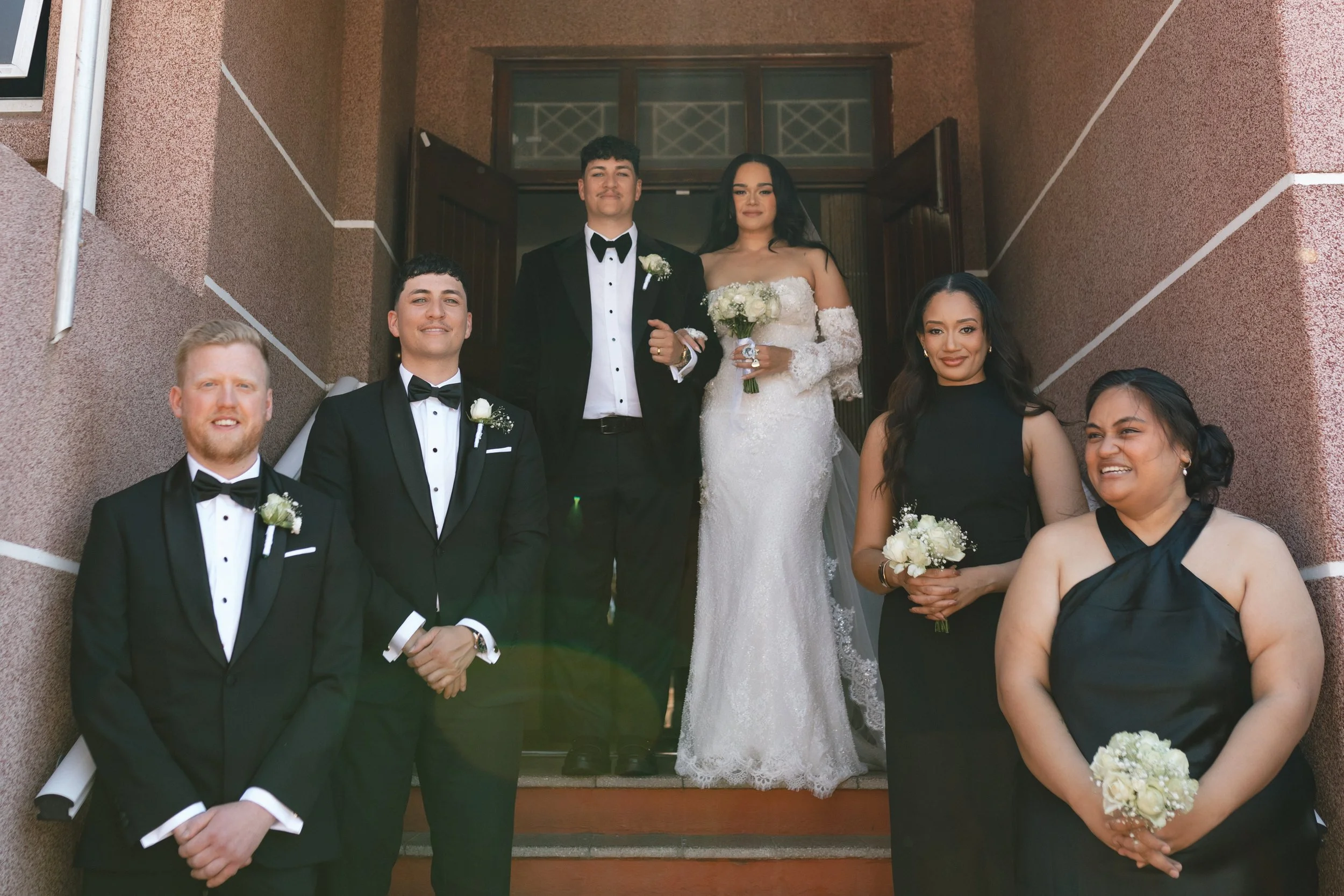 A group of six people, including a bride and groom, standing on steps outside a building, dressed in formal wedding attire. Gqeberha wedding photographer at Royalston Lakehouse.