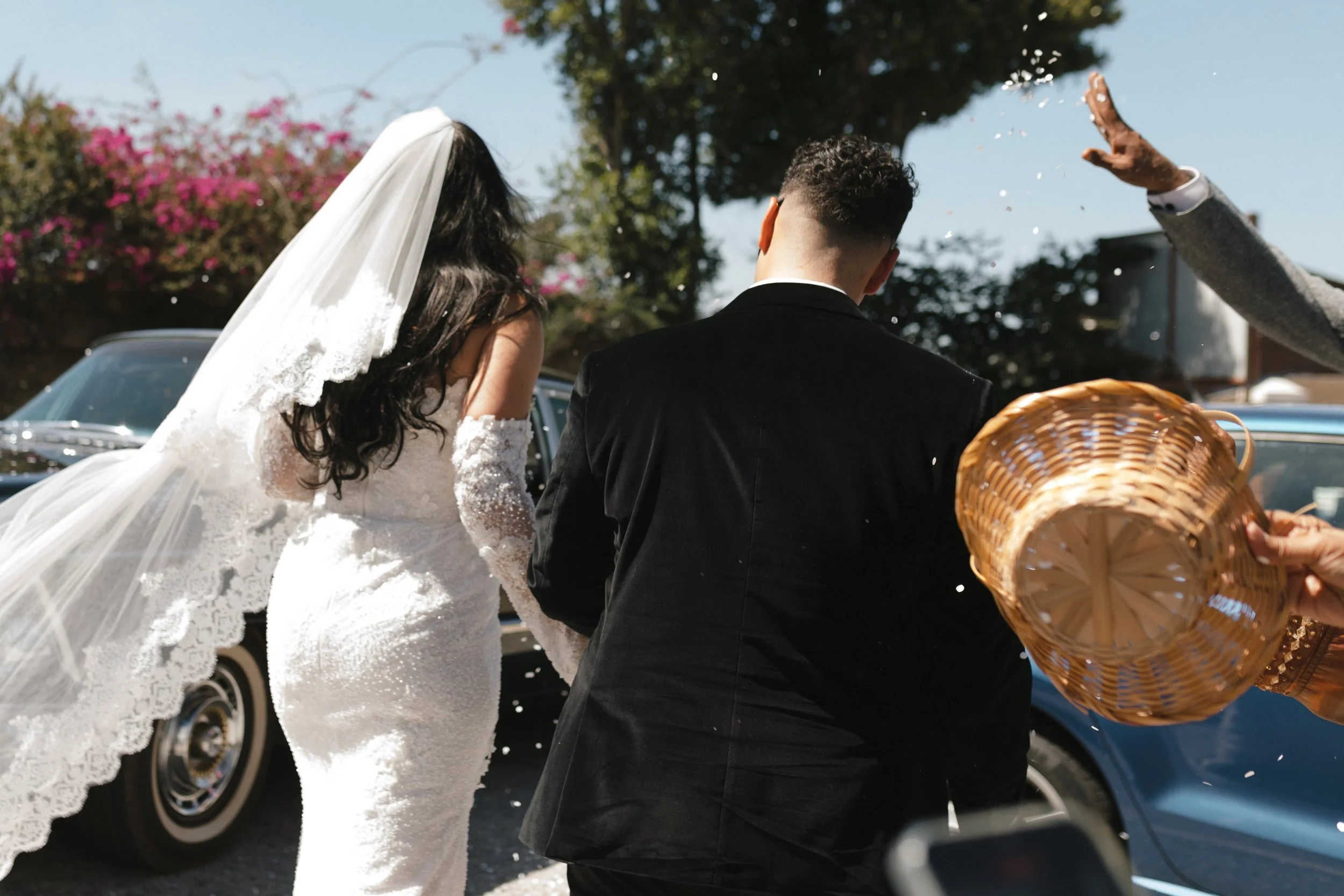 A bride and groom walking outdoors during daytime, with the bride in a white lace wedding dress and veil, and the groom in a black suit.  Gqeberha Slipperfields Wedding Venue